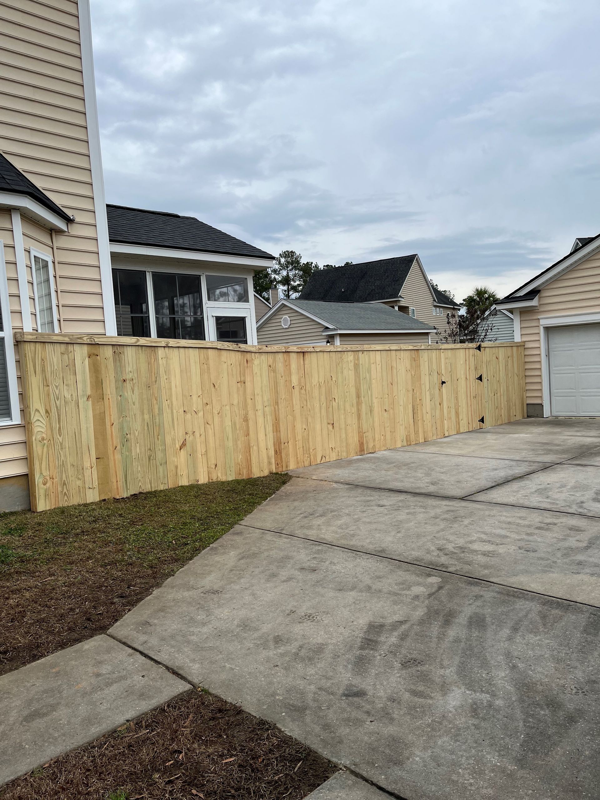 A wooden fence is surrounding a driveway in front of a house.