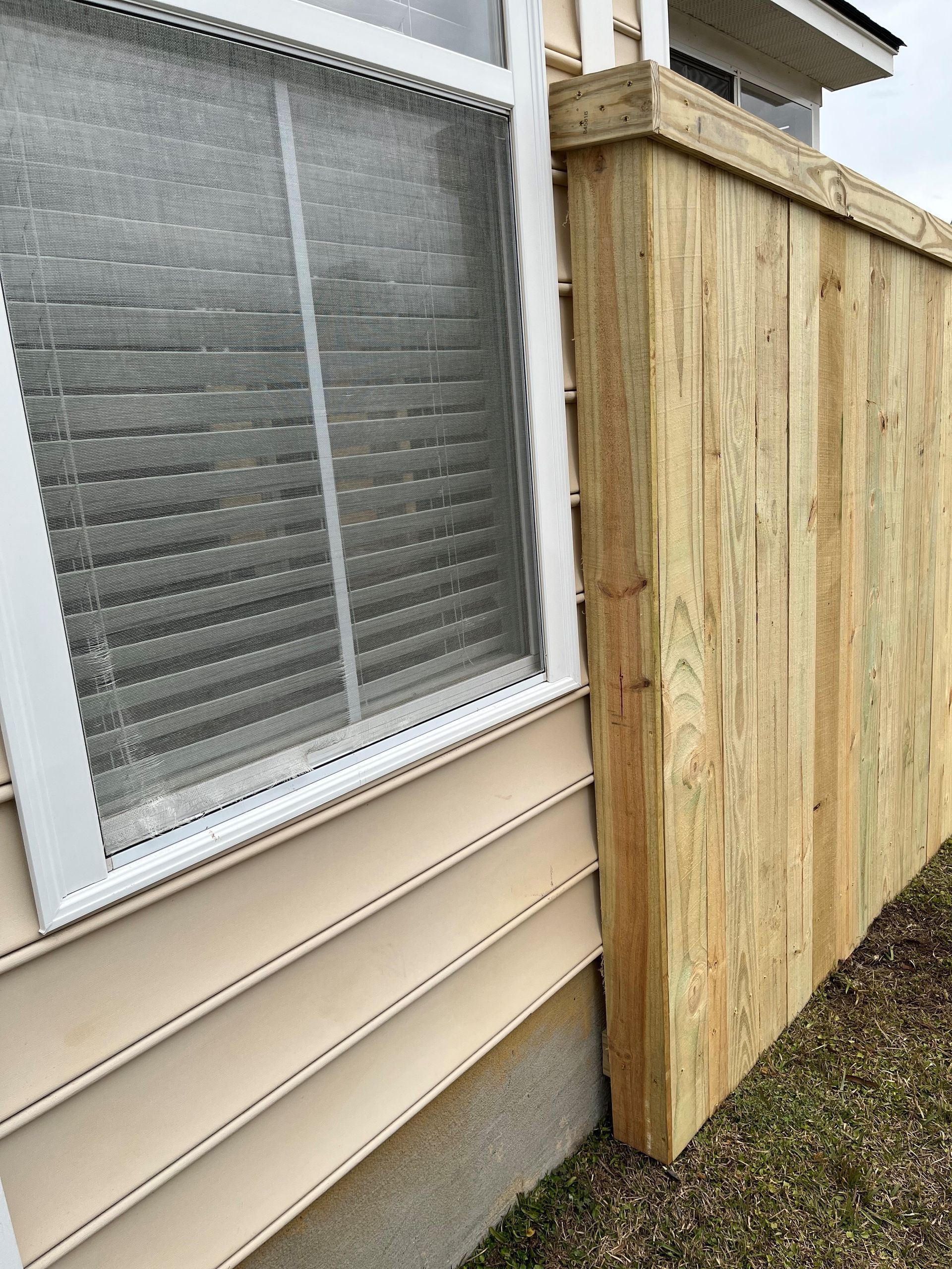A wooden fence is next to a window on the side of a house.