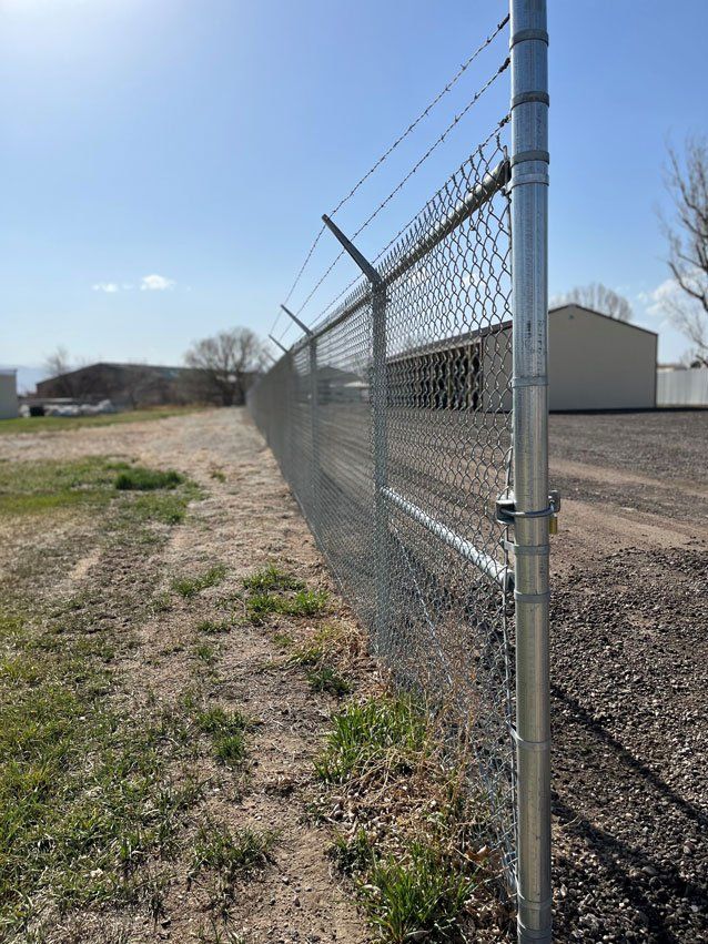 A chain link fence with barbed wire on top of it in a field.