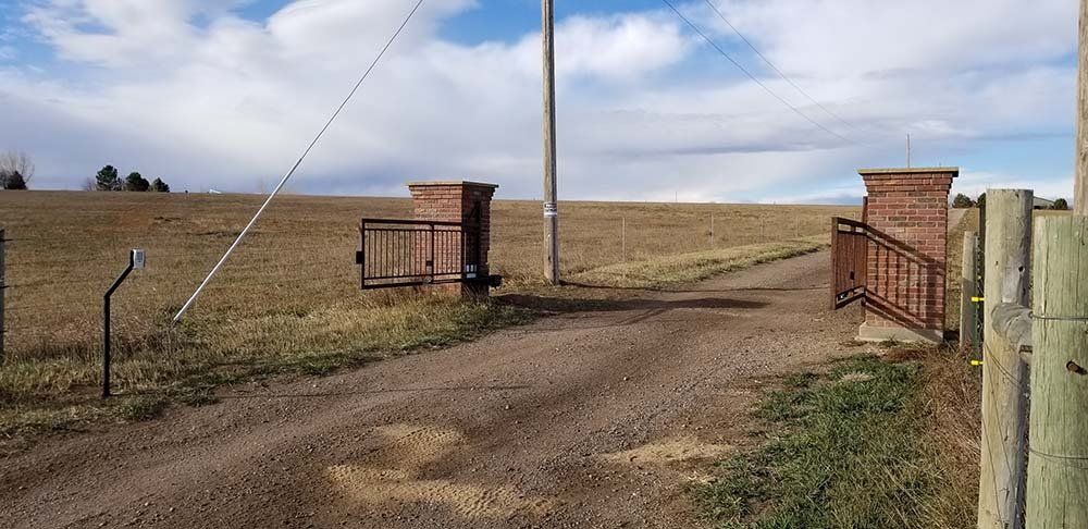 A dirt road with a gate in the middle of it leading to a field.