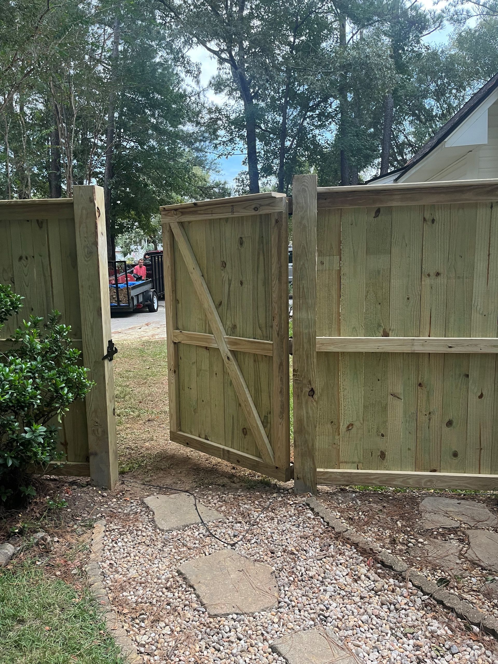 A wooden fence with a gate leading to a driveway.