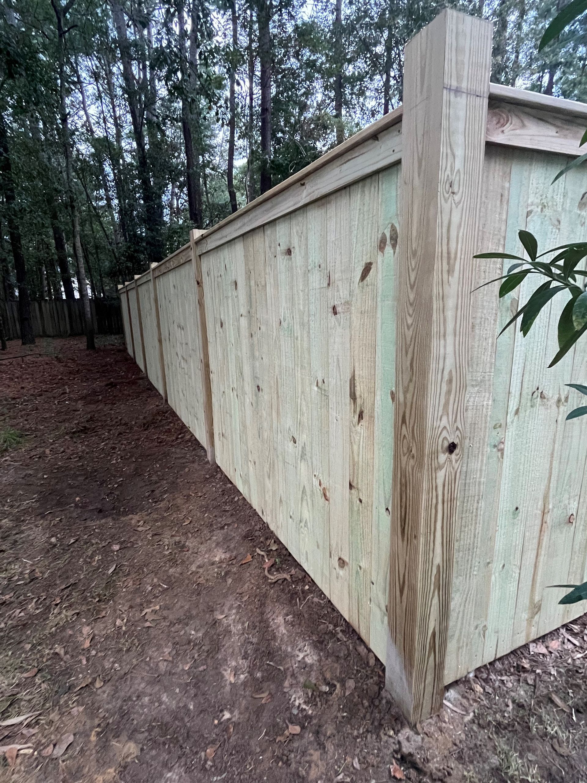 A wooden fence is sitting next to a dirt path in the woods.