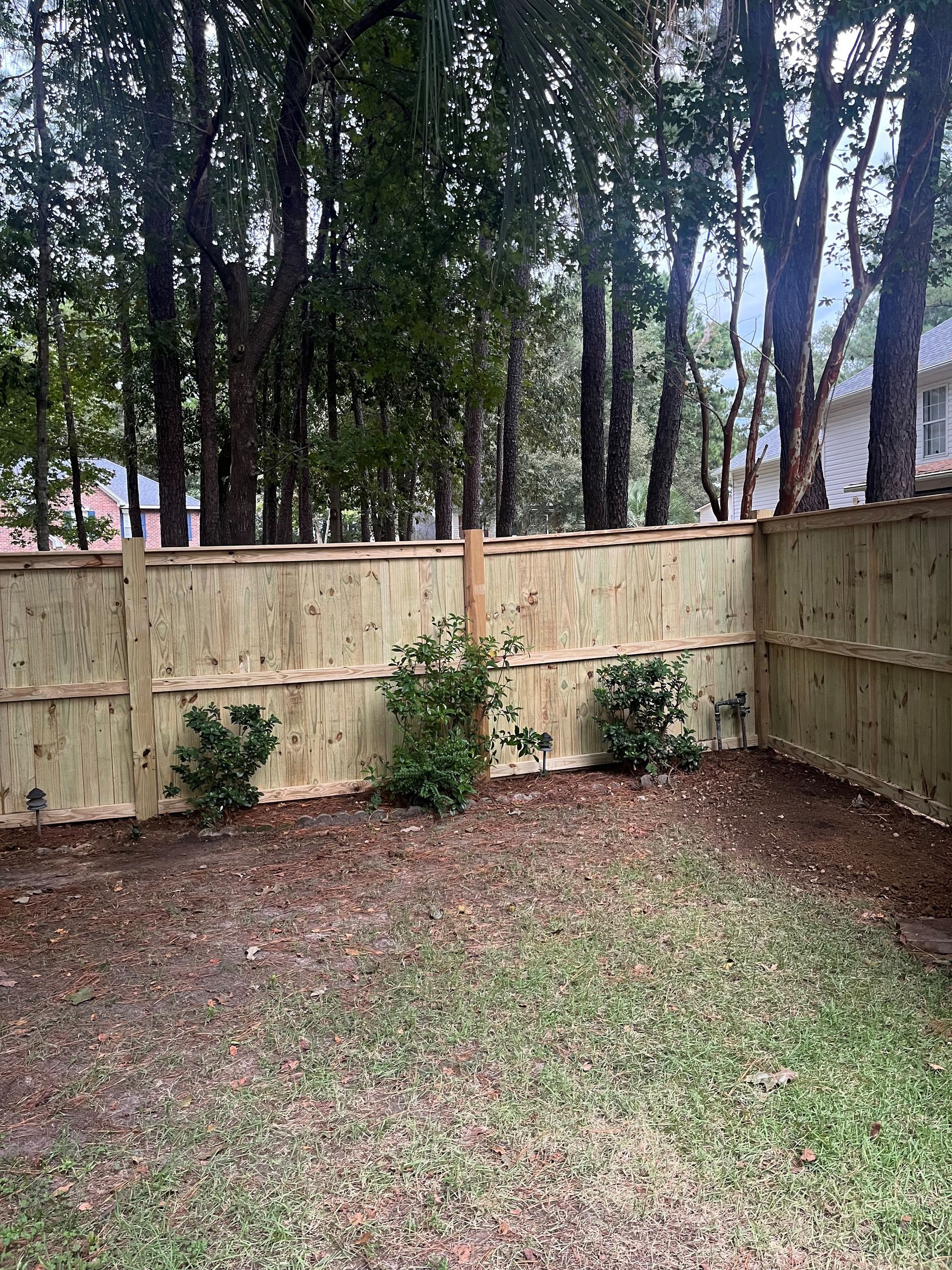 A wooden fence surrounds a backyard filled with grass and trees.
