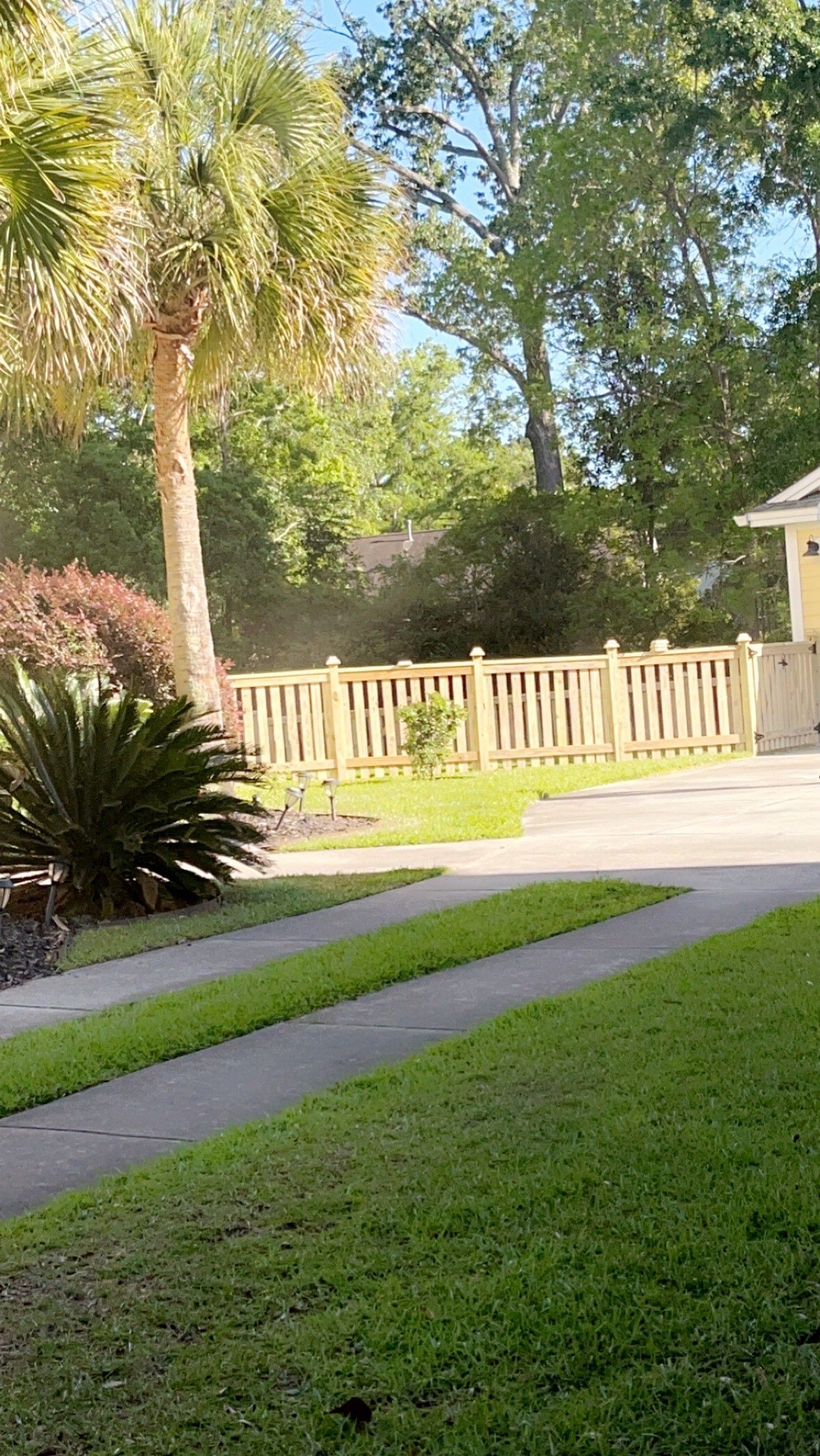 A white fence surrounds a lush green yard in front of a house.