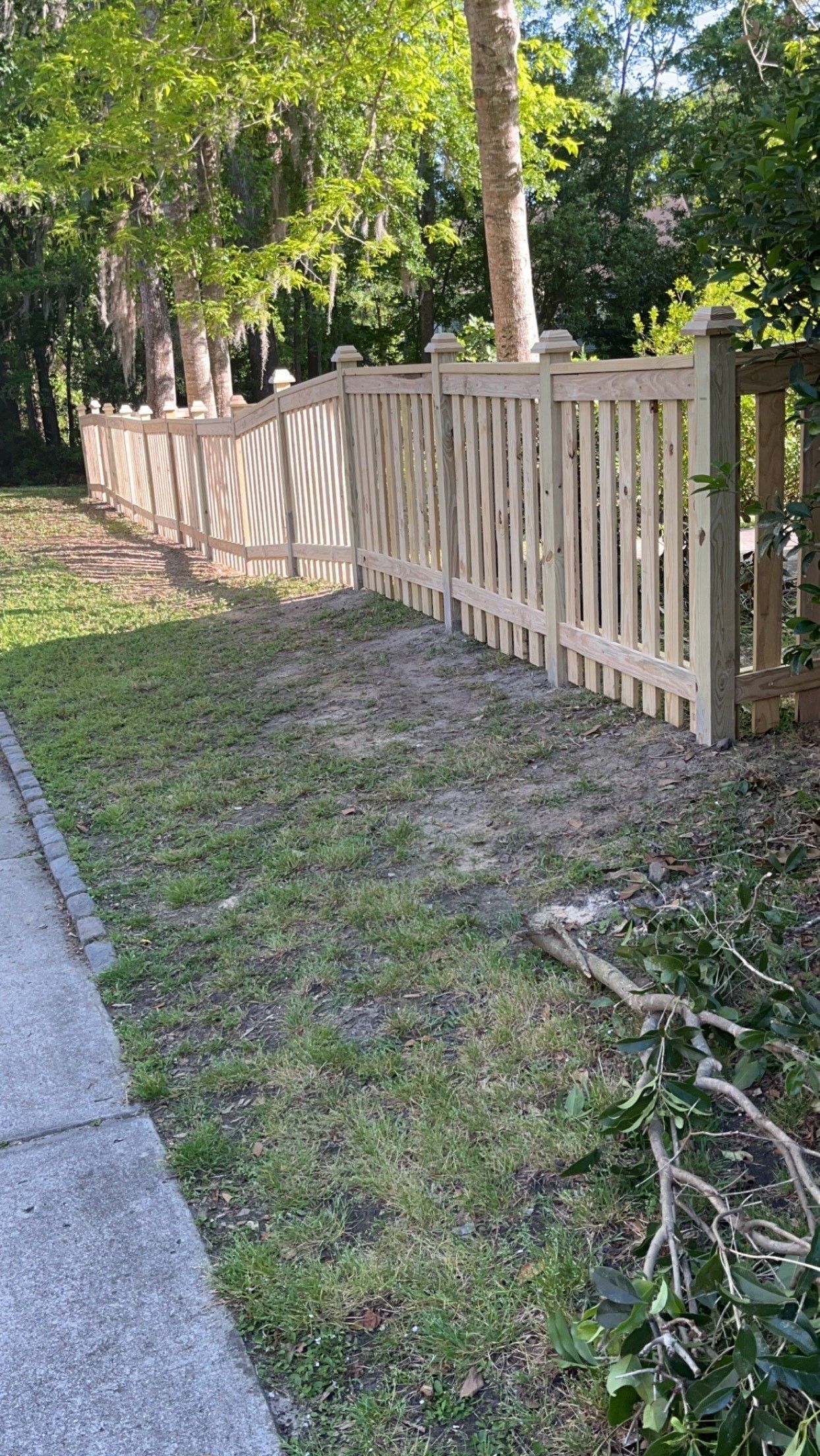 A wooden fence surrounds a grassy area next to a sidewalk.