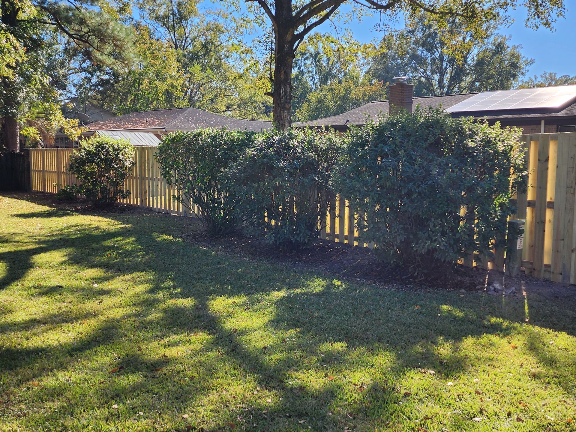 A wooden fence surrounds a lush green yard with a house in the background.