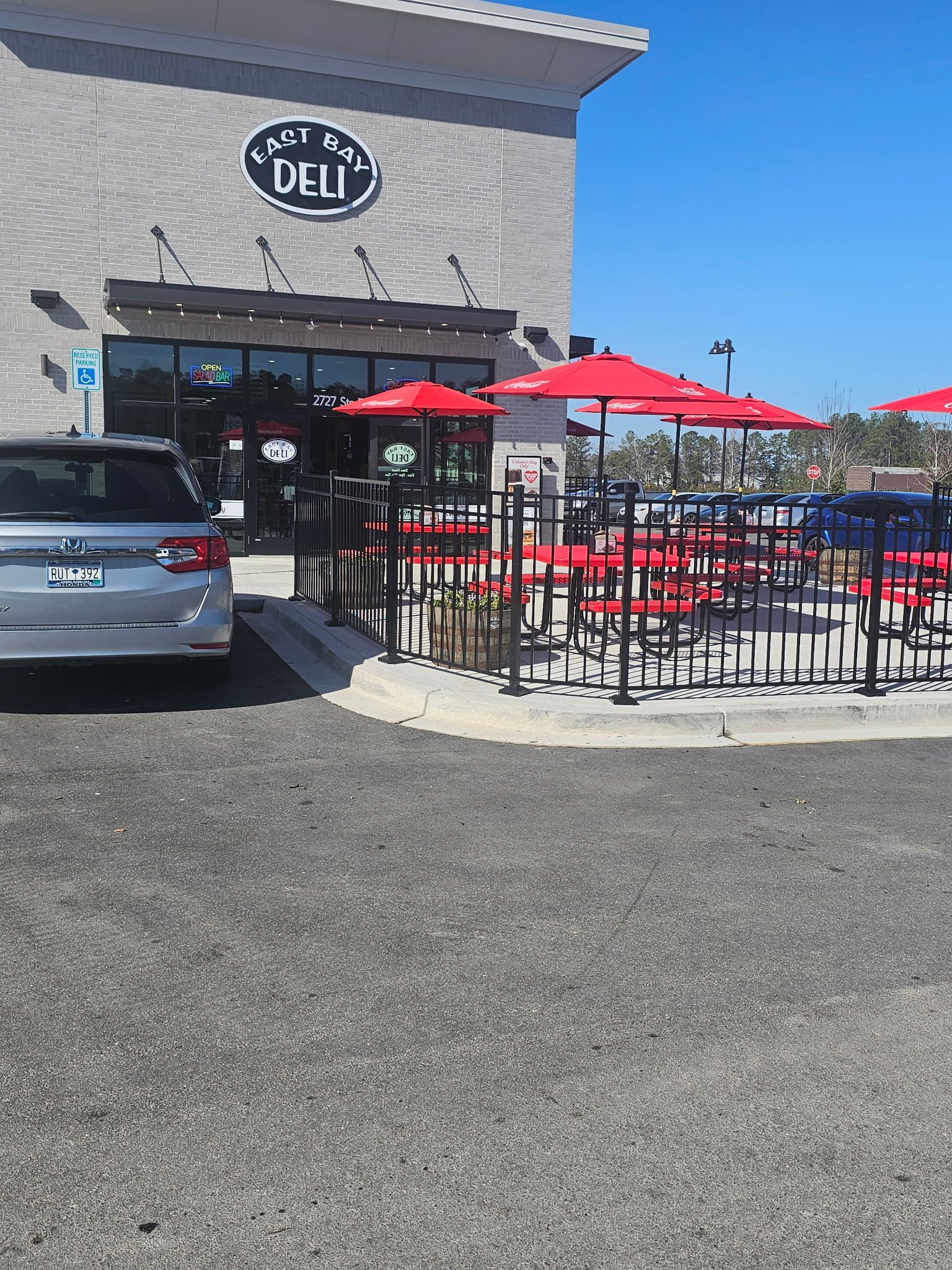A car is parked in front of a restaurant with tables and umbrellas.