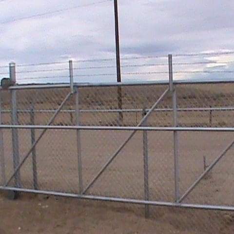 A chain link fence is surrounding a dirt field.