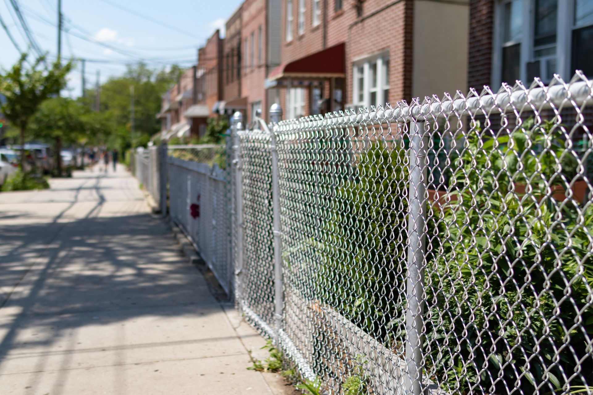 A chain link fence along a sidewalk in a residential neighborhood.