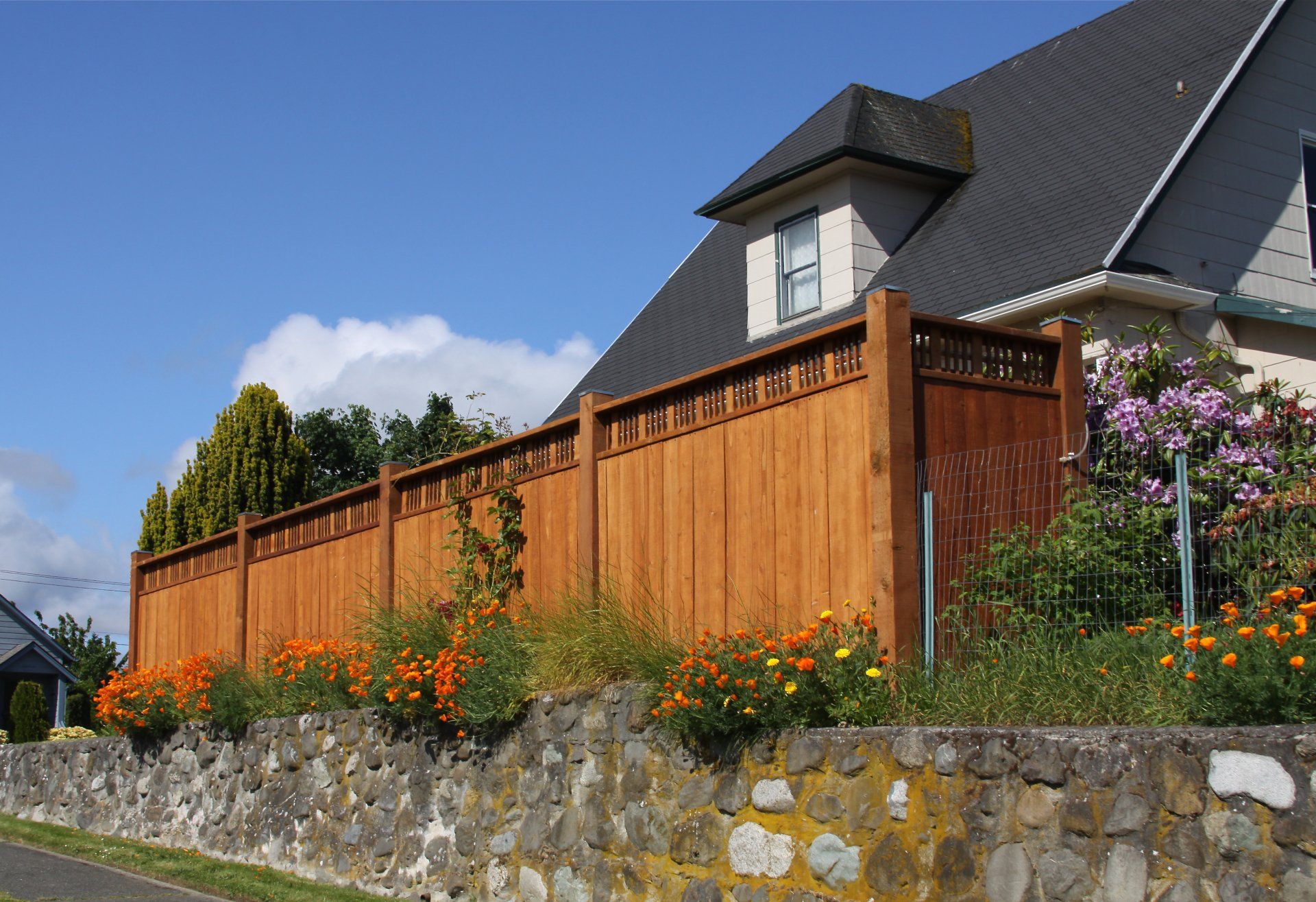 A wooden fence surrounds a stone wall in front of a house
