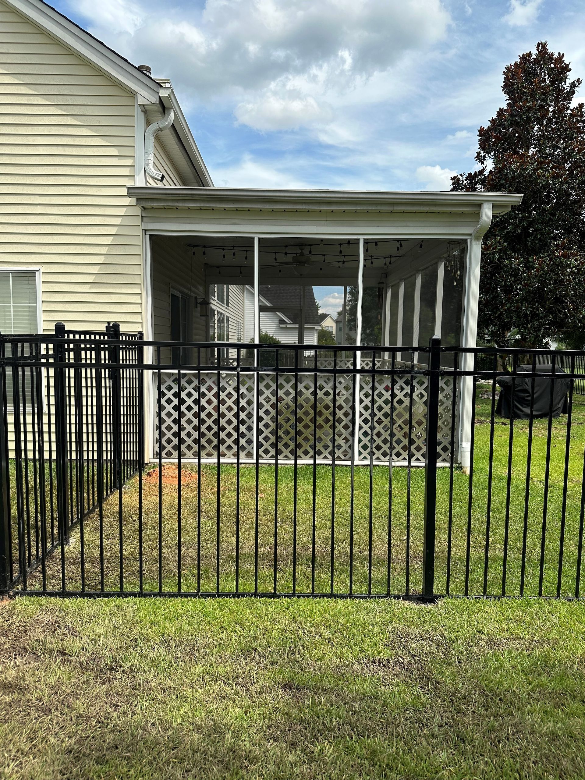 A house with a screened in porch and a black fence in front of it.