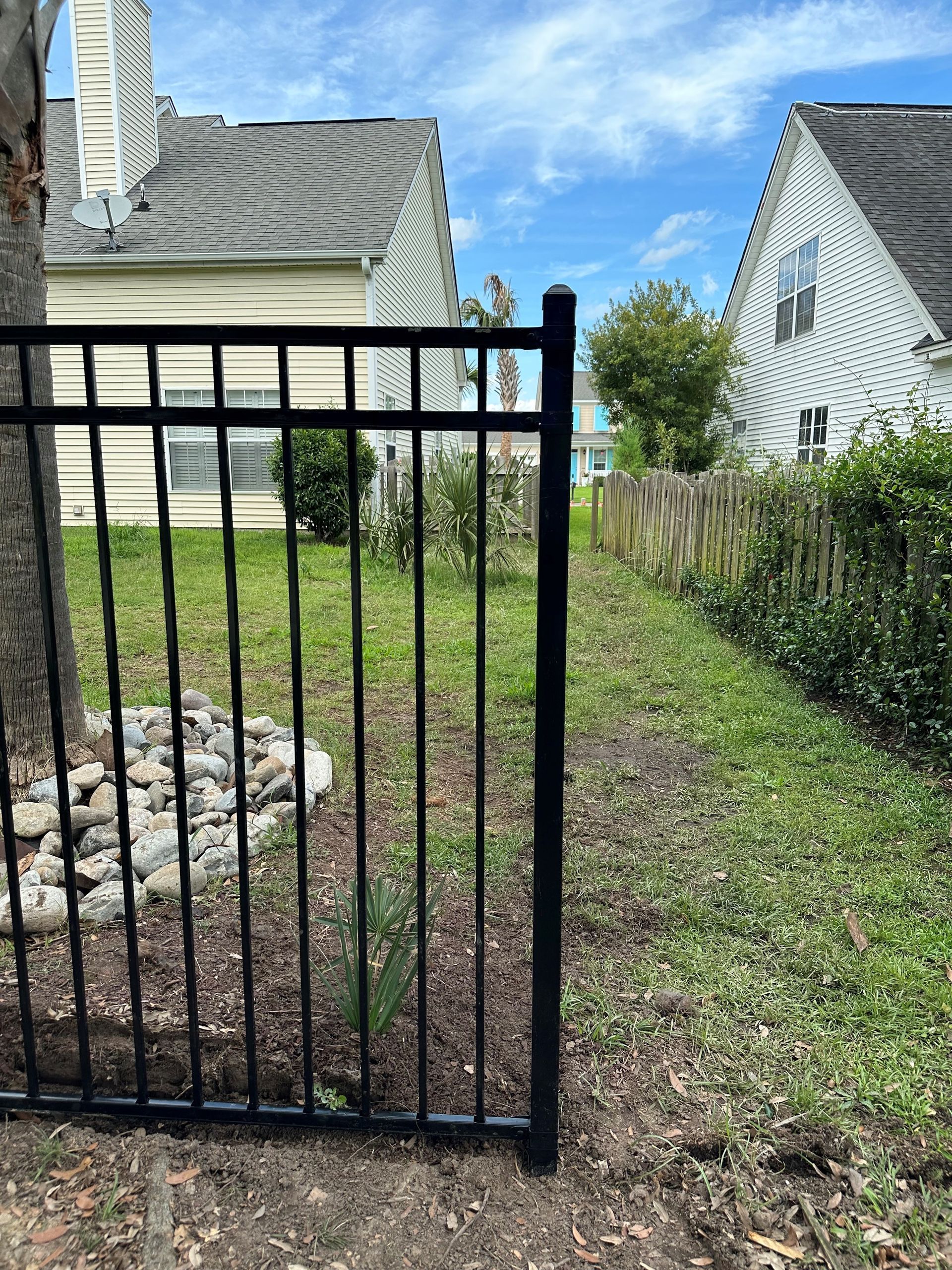 A black fence is surrounding a yard with a house in the background.