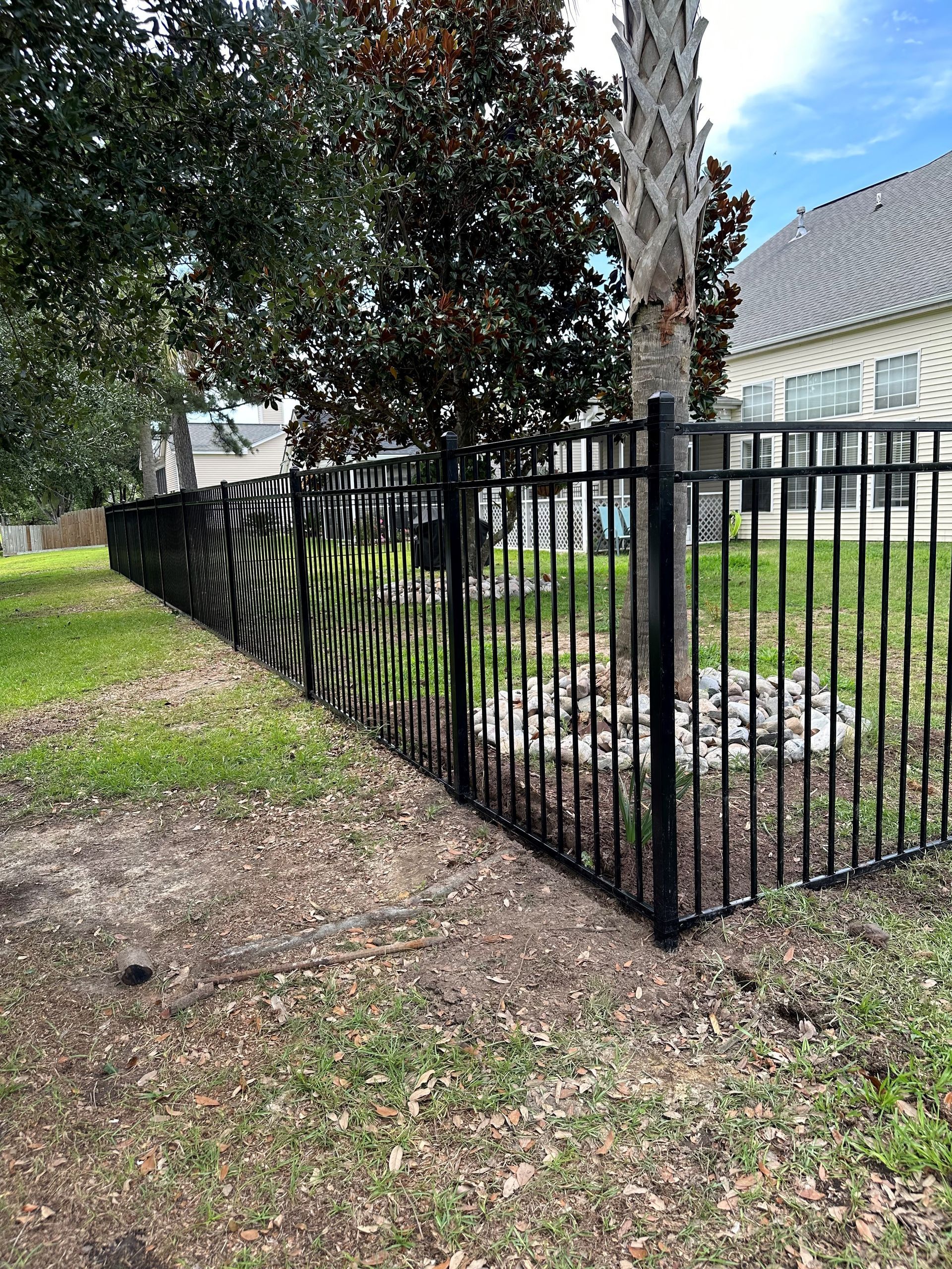 A black fence surrounds a lush green yard in front of a house.