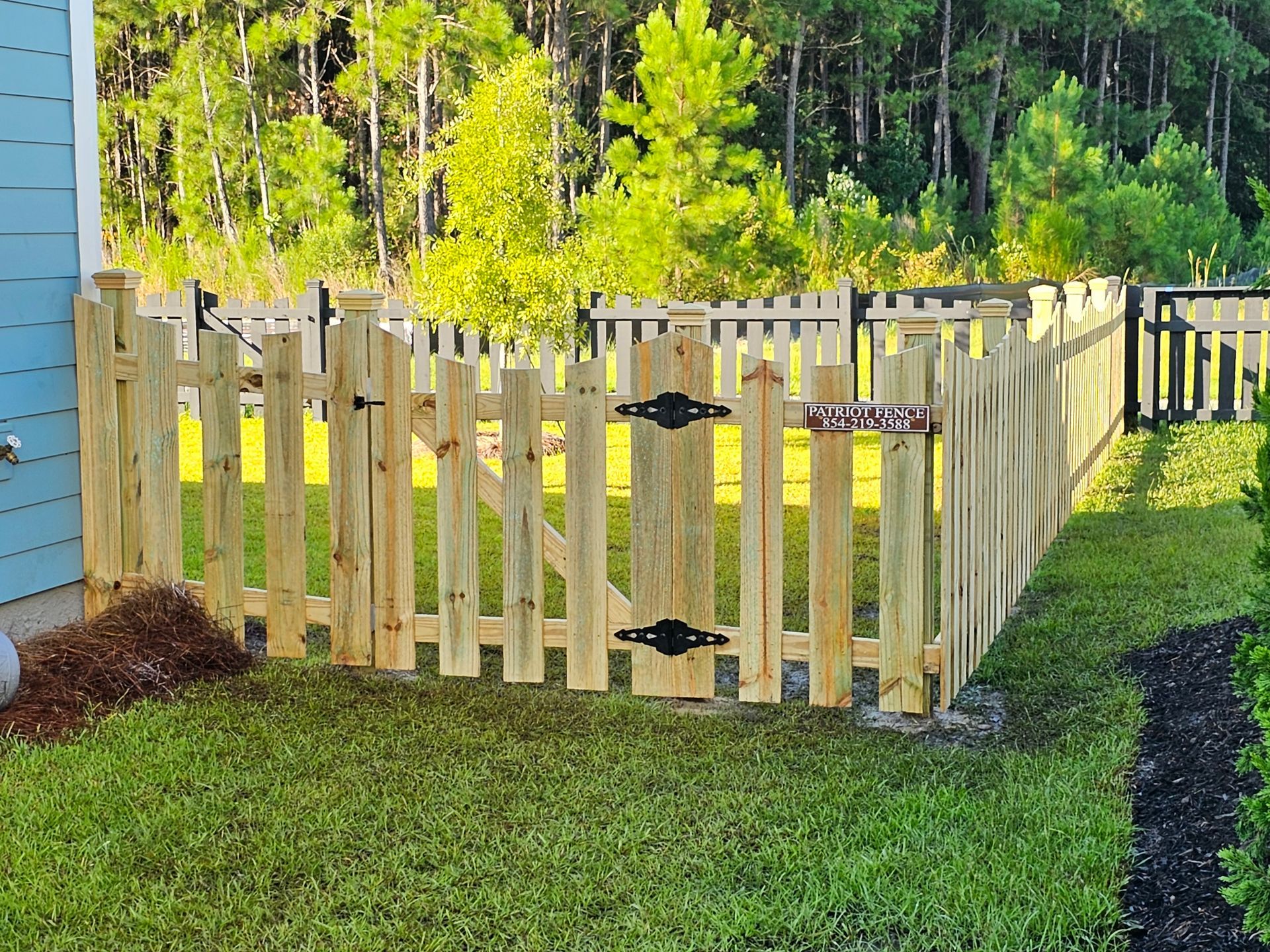 A wooden picket fence with a gate in the backyard of a house.