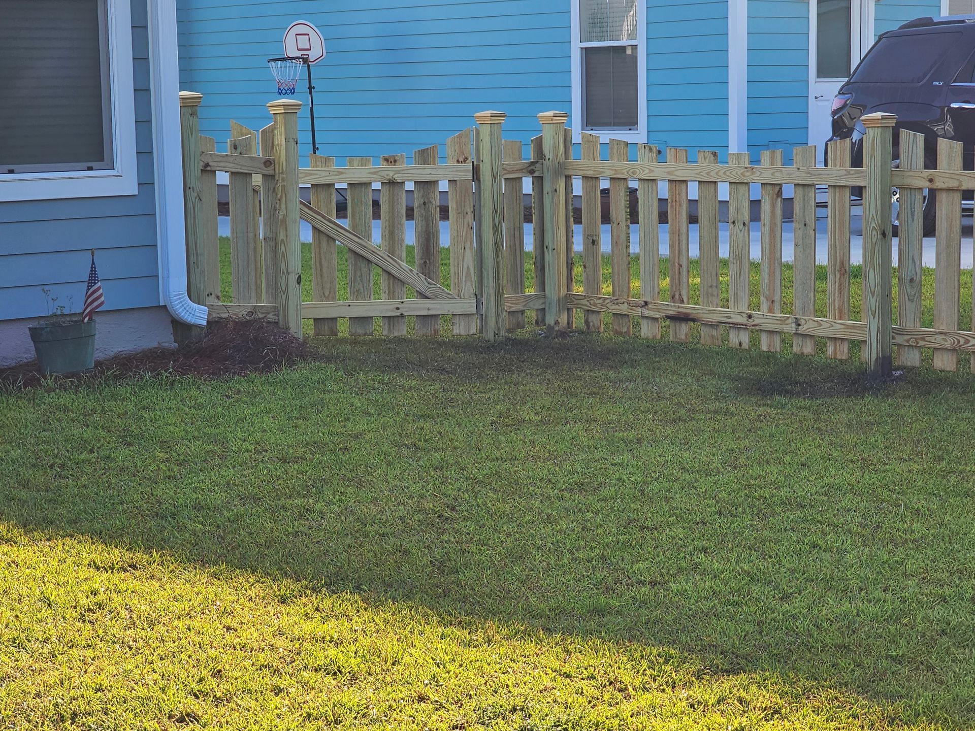A wooden picket fence surrounds a lush green lawn in front of a blue house.
