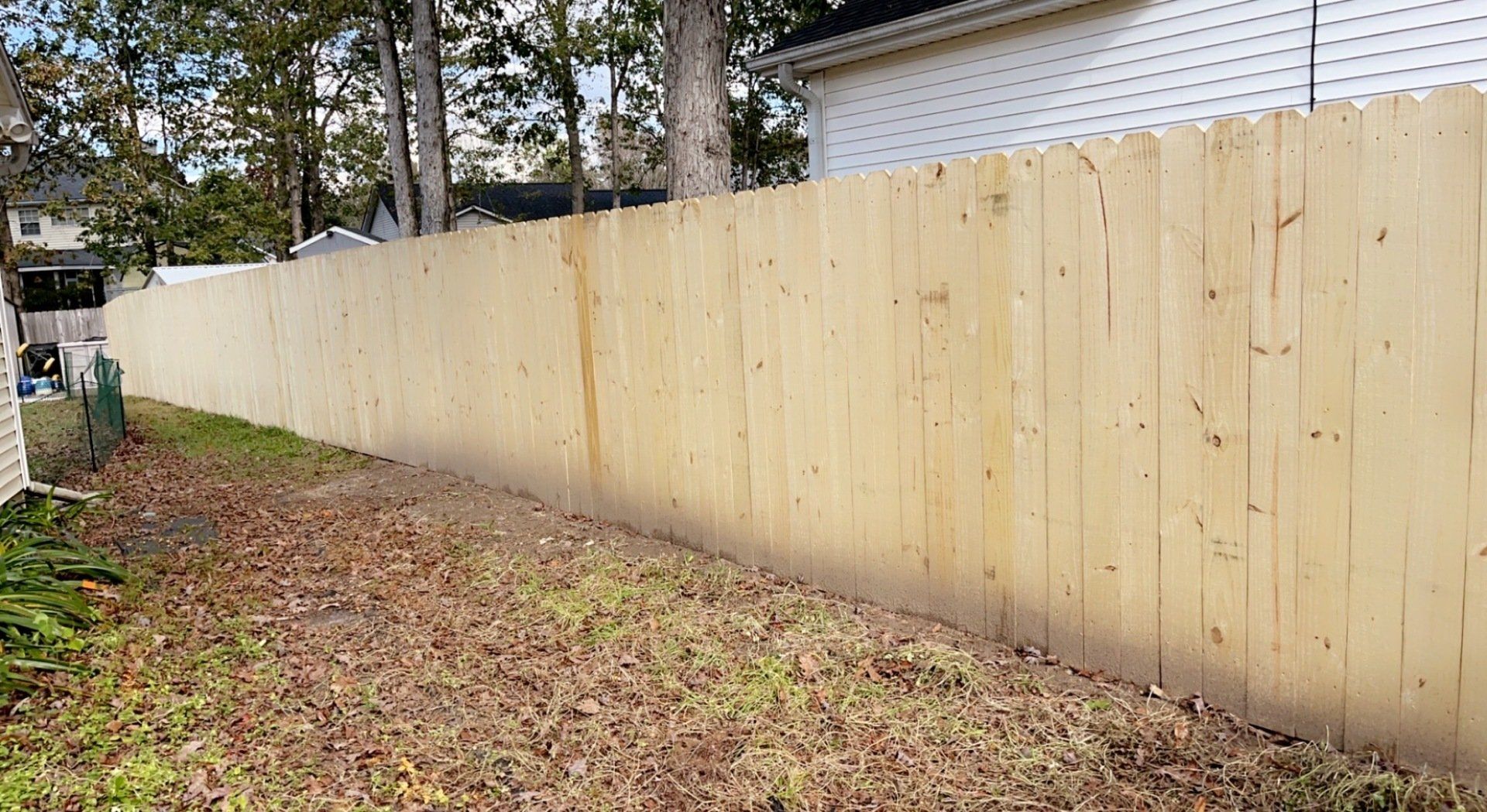 A long wooden fence surrounds a yard with a house in the background.