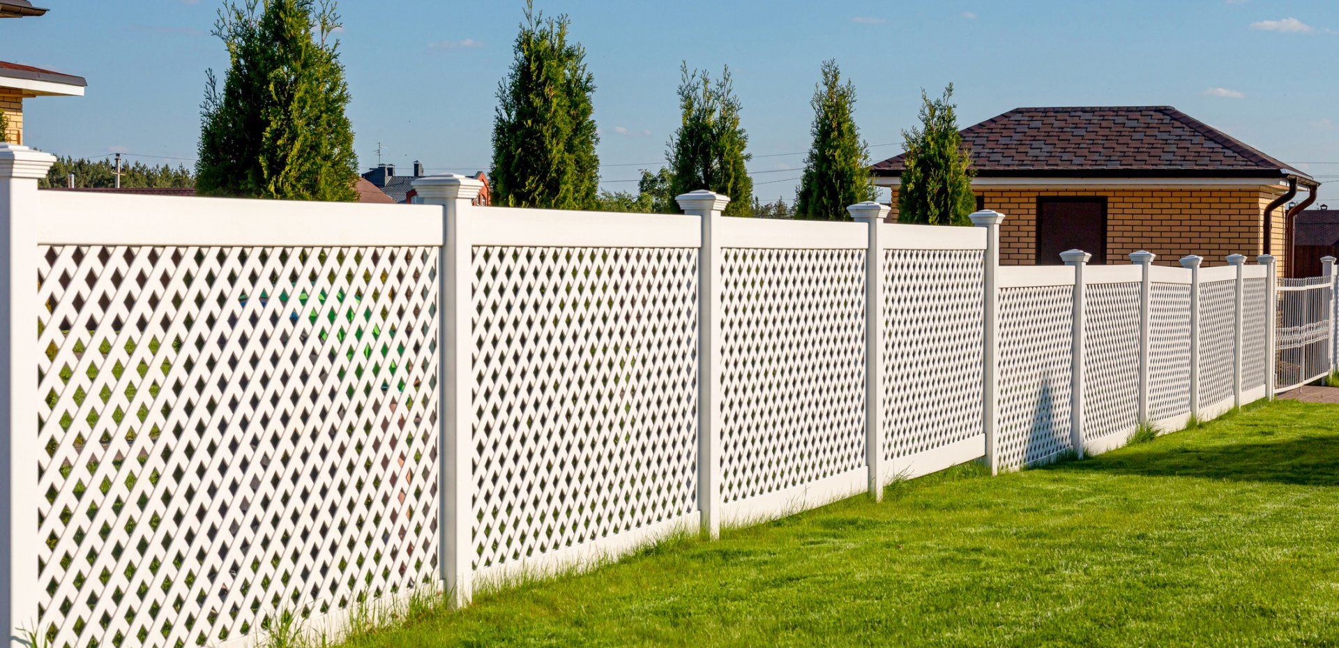 A white lattice fence surrounds a lush green lawn in front of a house.