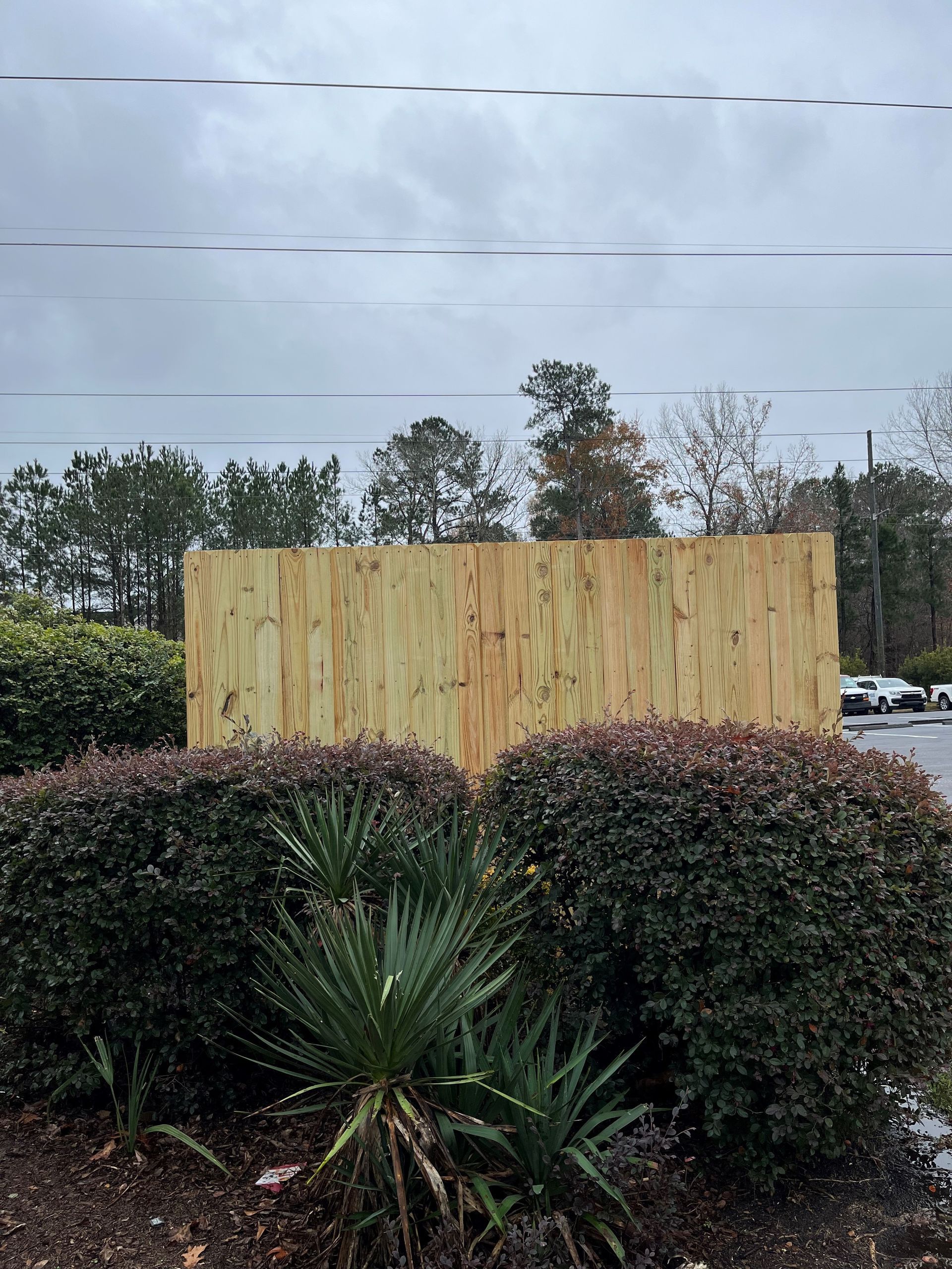 A wooden fence is surrounded by bushes and trees on a cloudy day.