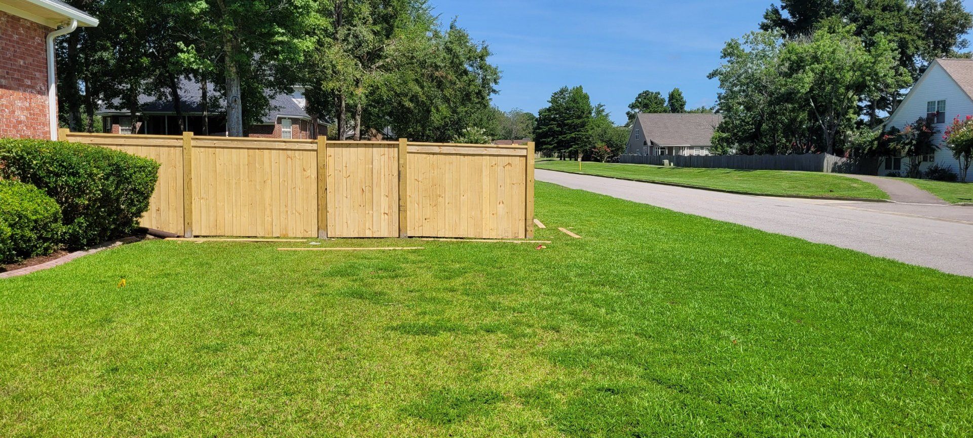 A wooden fence surrounds a lush green lawn in a residential neighborhood.