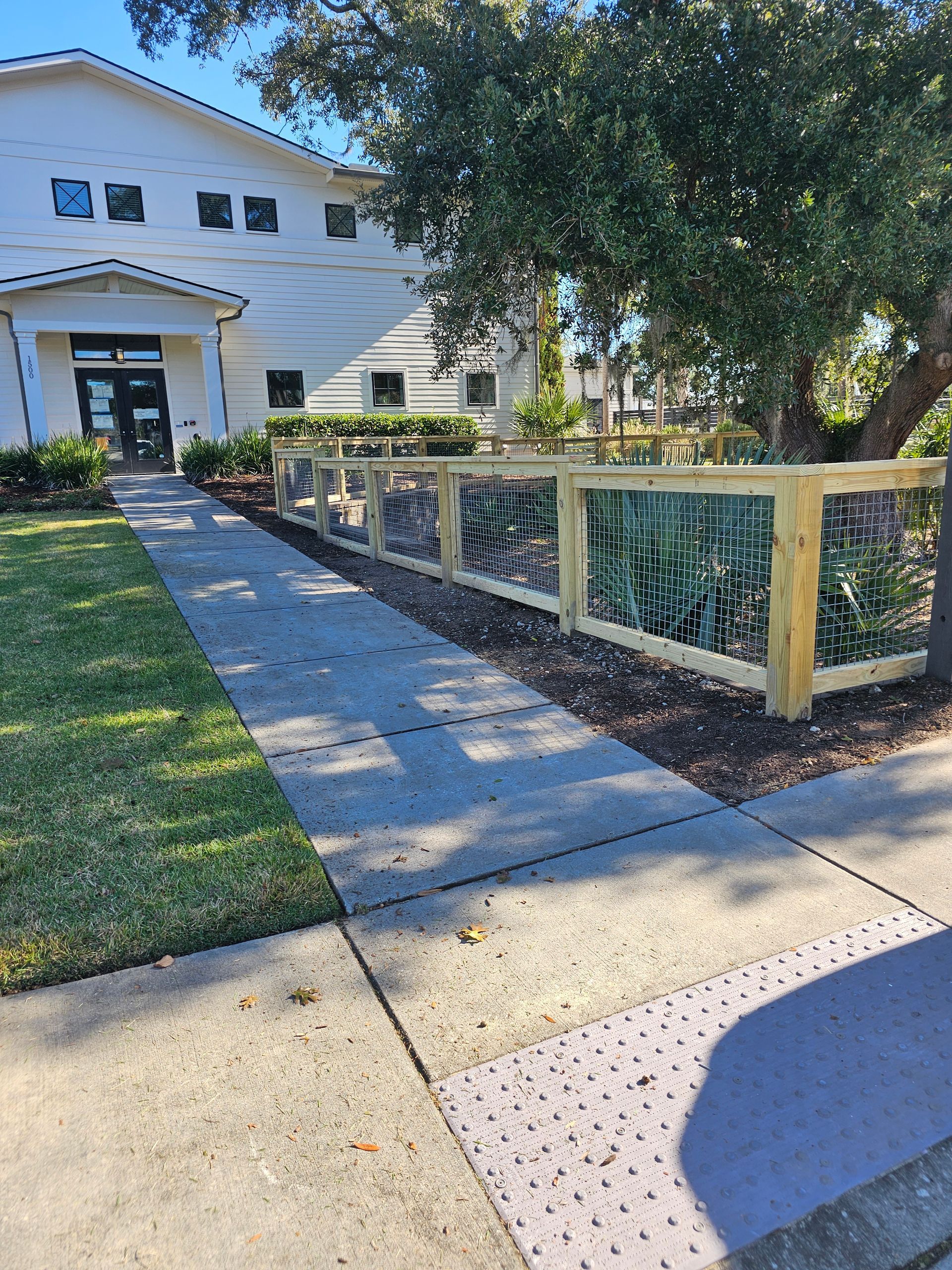 A wooden fence surrounds a sidewalk in front of a white building.
