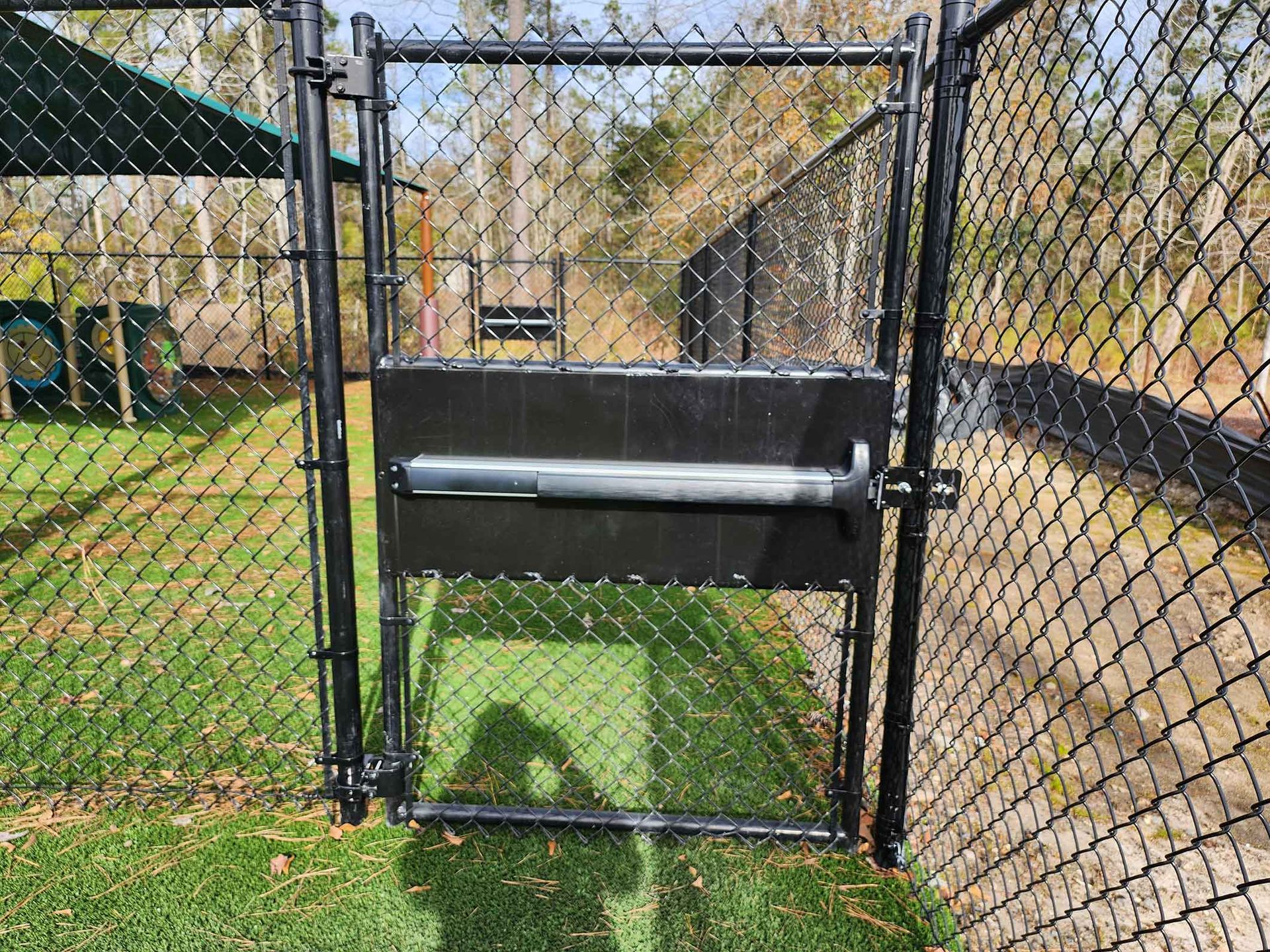 A chain link fence with a gate leading to a playground.