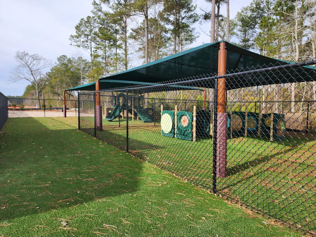 A chain link fence surrounds a playground with a canopy over it.