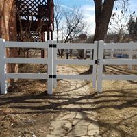 A white fence with a gate is sitting next to a stone walkway.