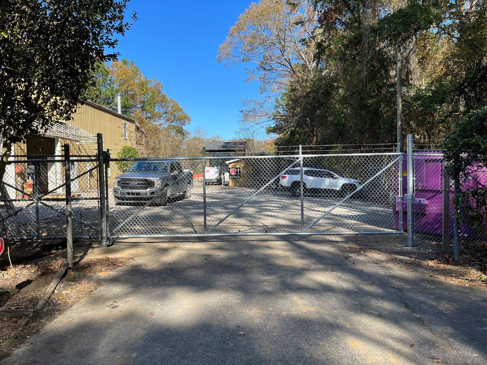 A chain link fence surrounds a parking lot with cars parked in front of it.