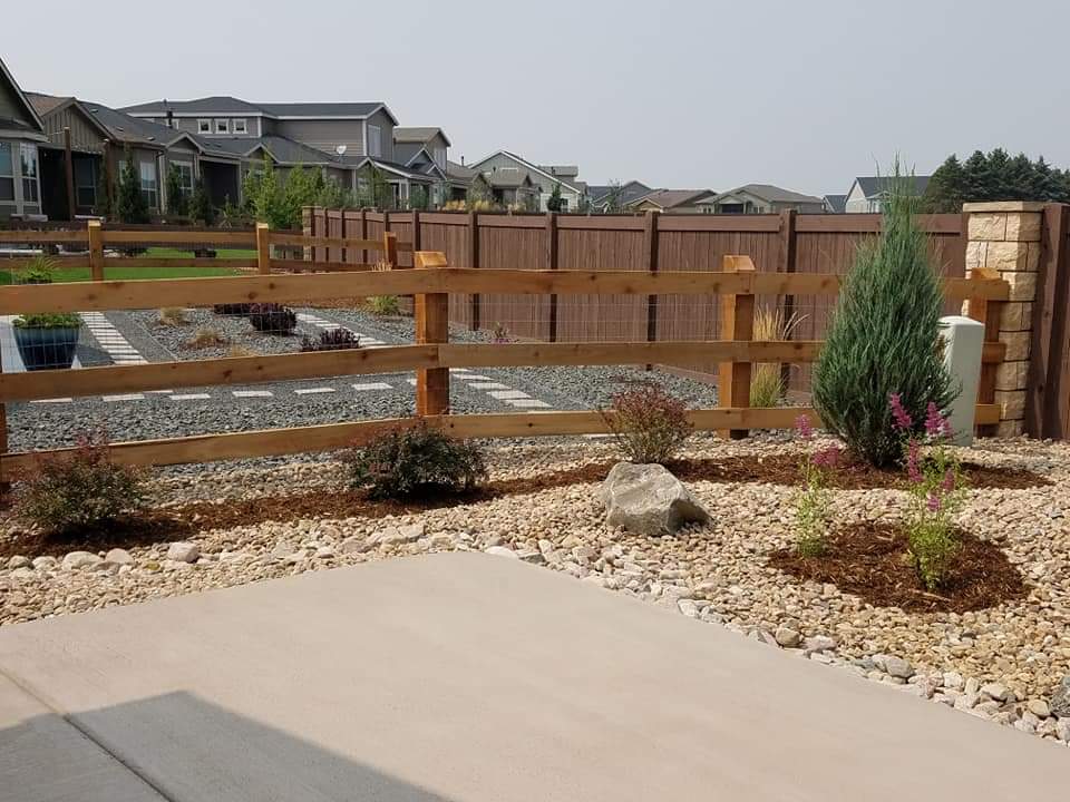 A wooden fence is surrounded by rocks and plants