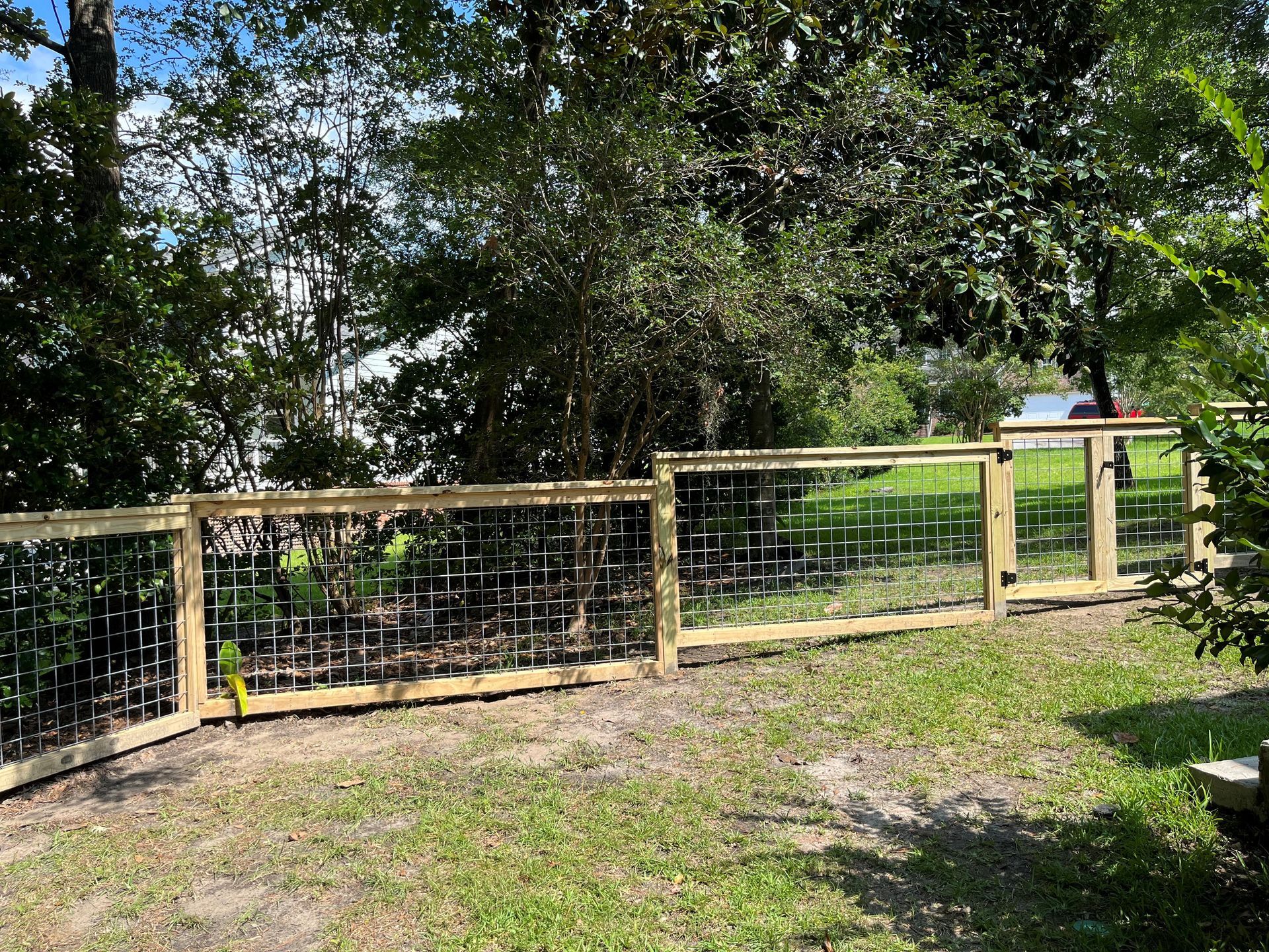 A wooden fence is surrounded by trees and grass in a yard.