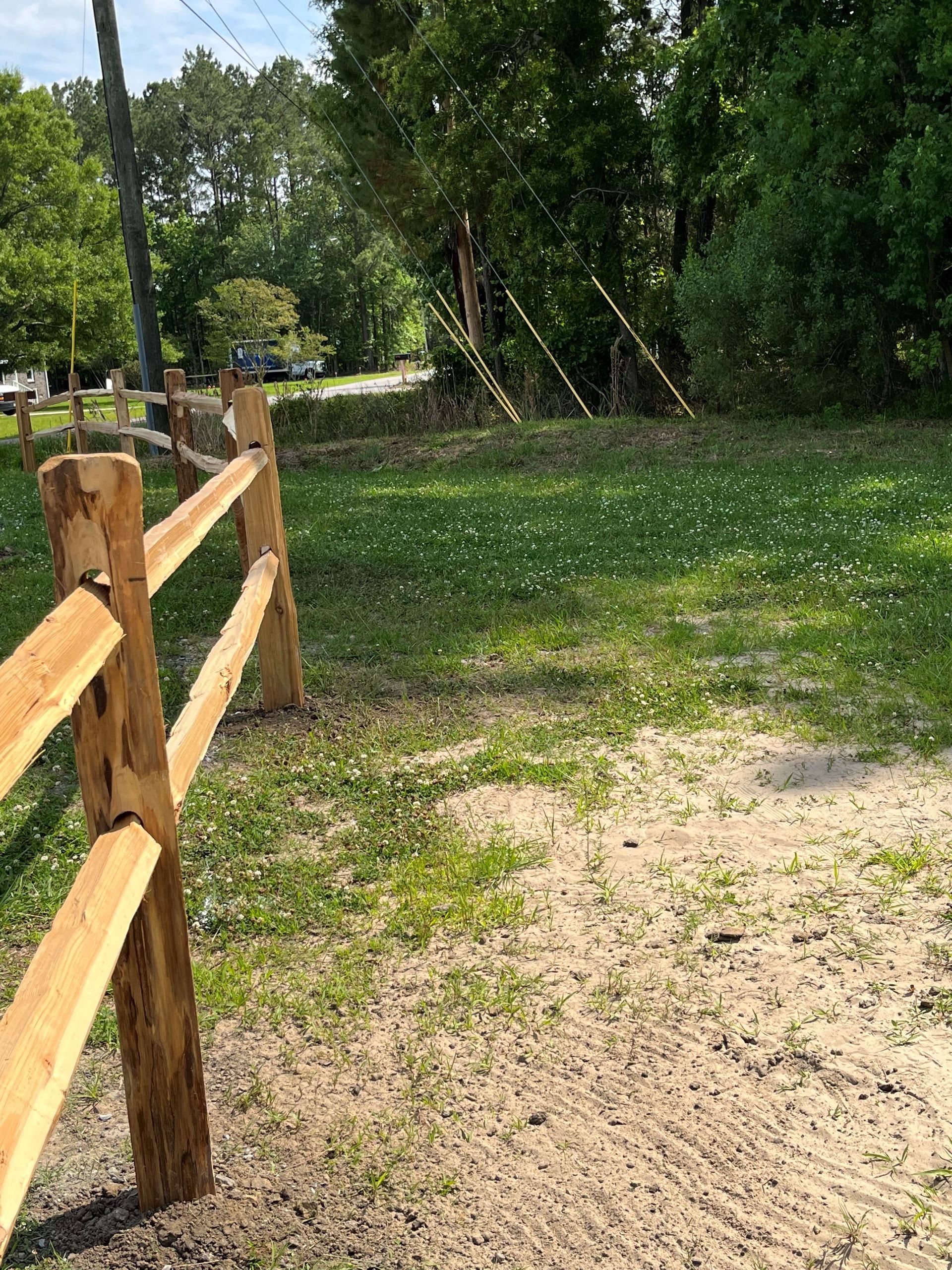 A wooden fence surrounds a grassy field with trees in the background.