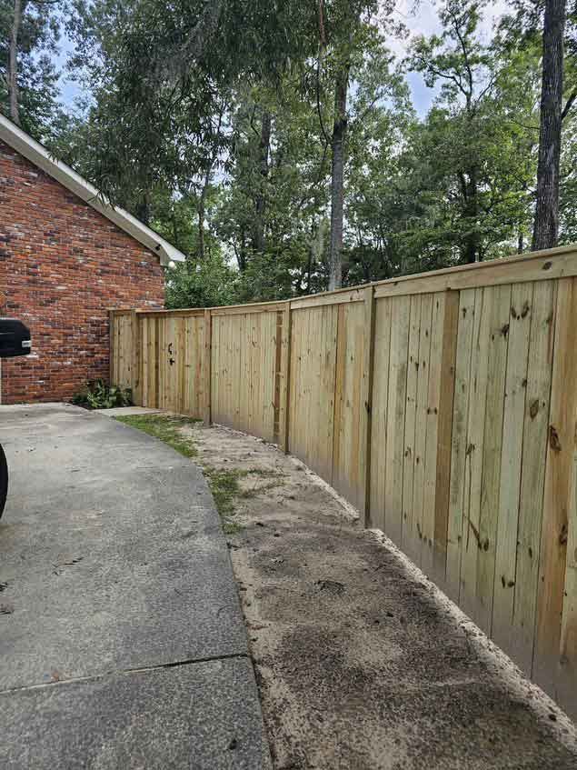 A wooden fence is sitting on the side of a driveway next to a brick house.