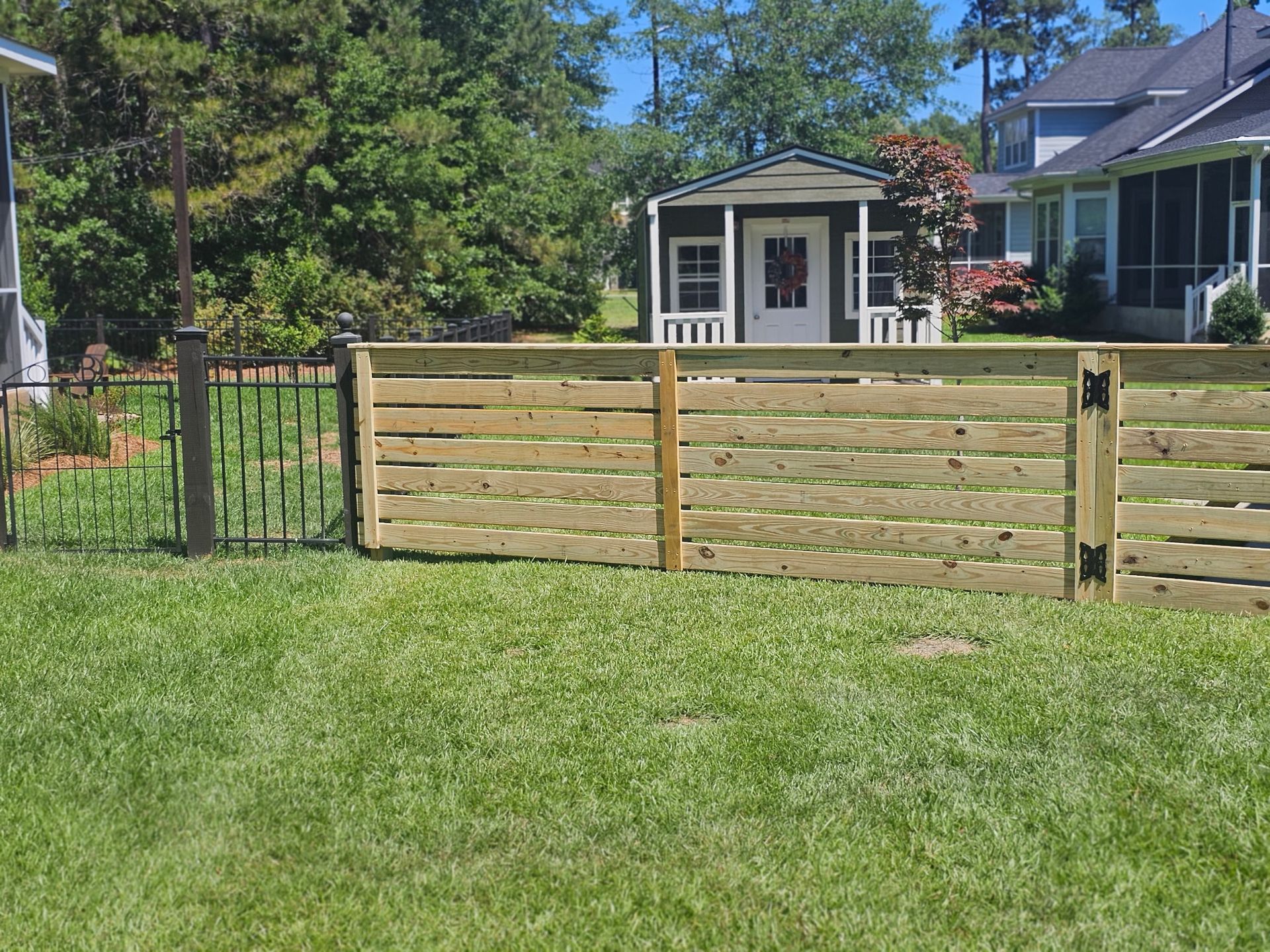 A wooden fence surrounds a lush green yard in front of a house.