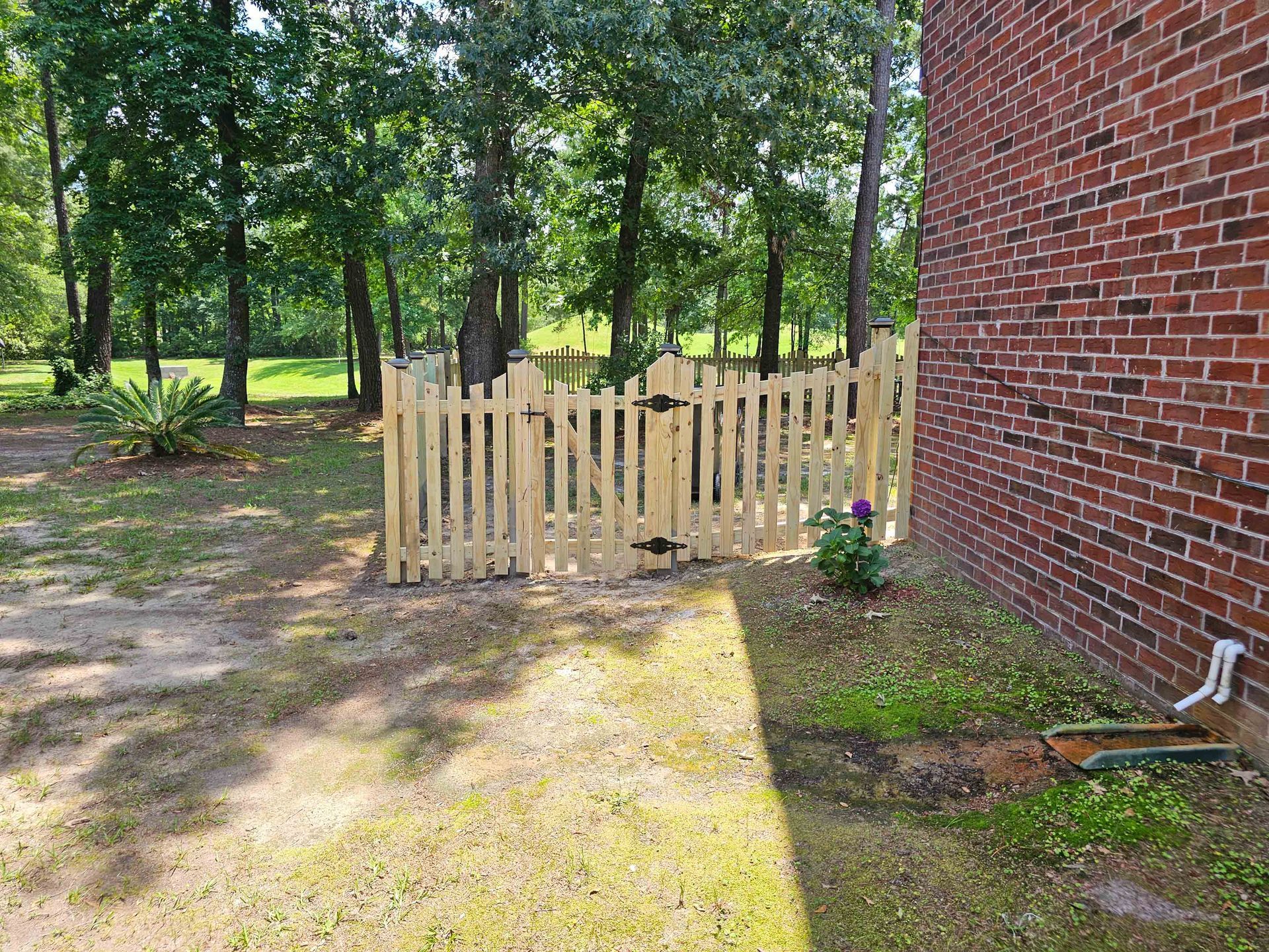 A wooden picket fence is sitting next to a brick wall in a yard.