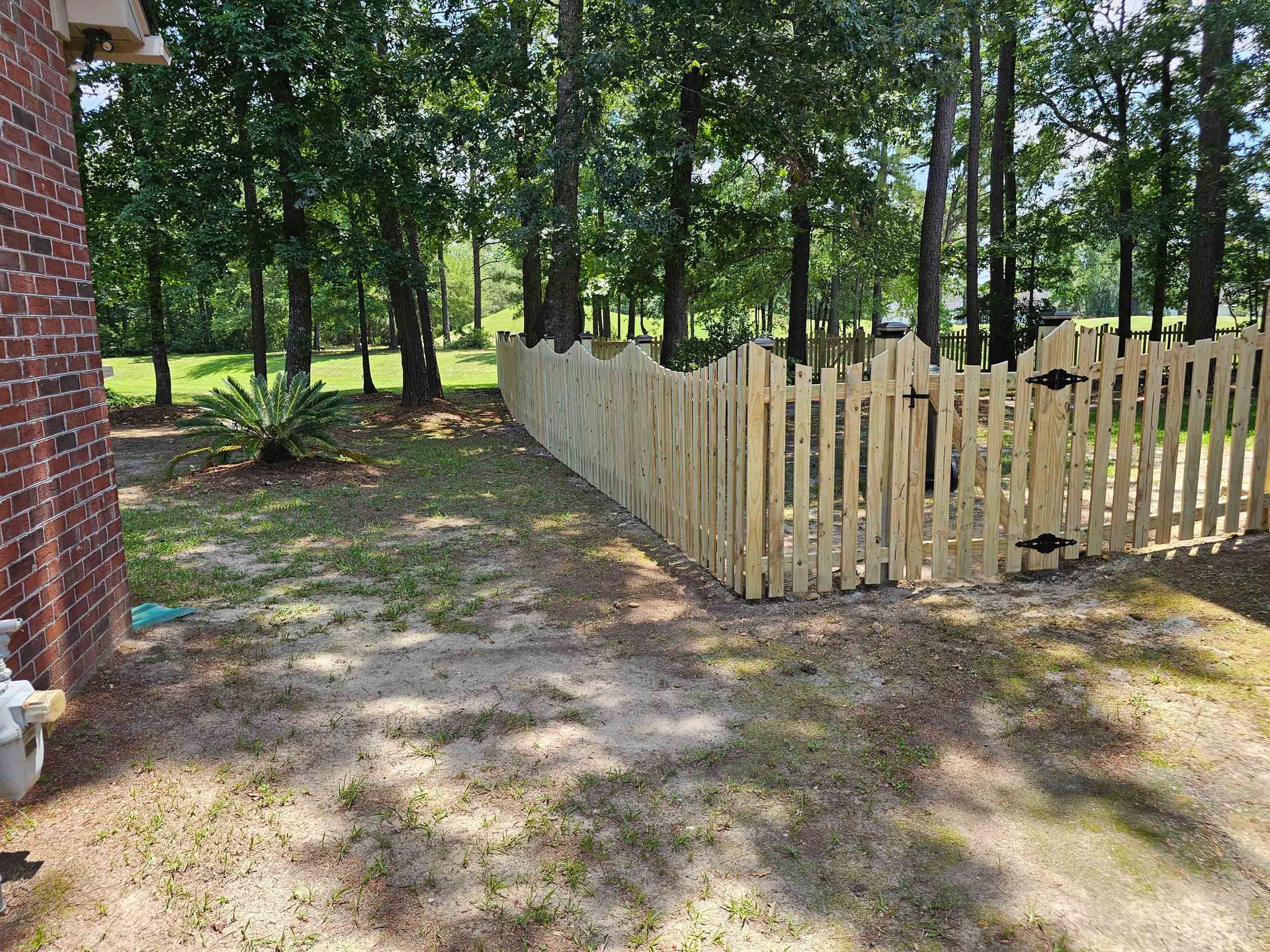 A wooden picket fence is surrounded by trees in a backyard.