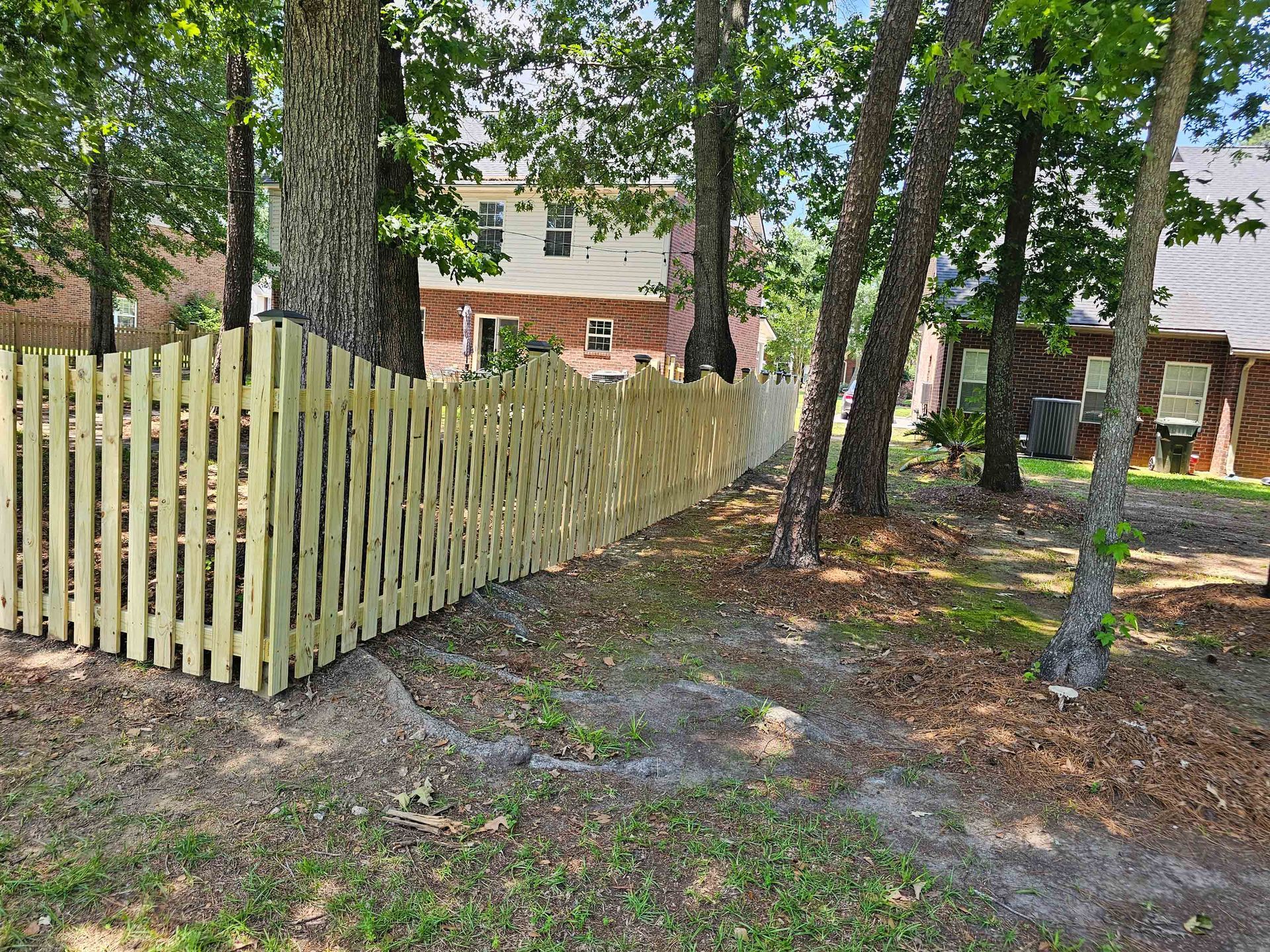 A wooden picket fence is surrounded by trees in front of a house.