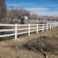 A white fence surrounds a dirt field with a barn in the background.