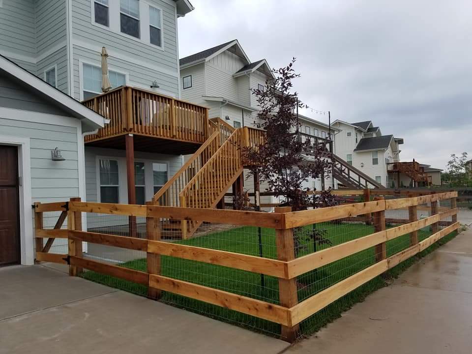 A wooden fence surrounds a lush green yard in front of a house.