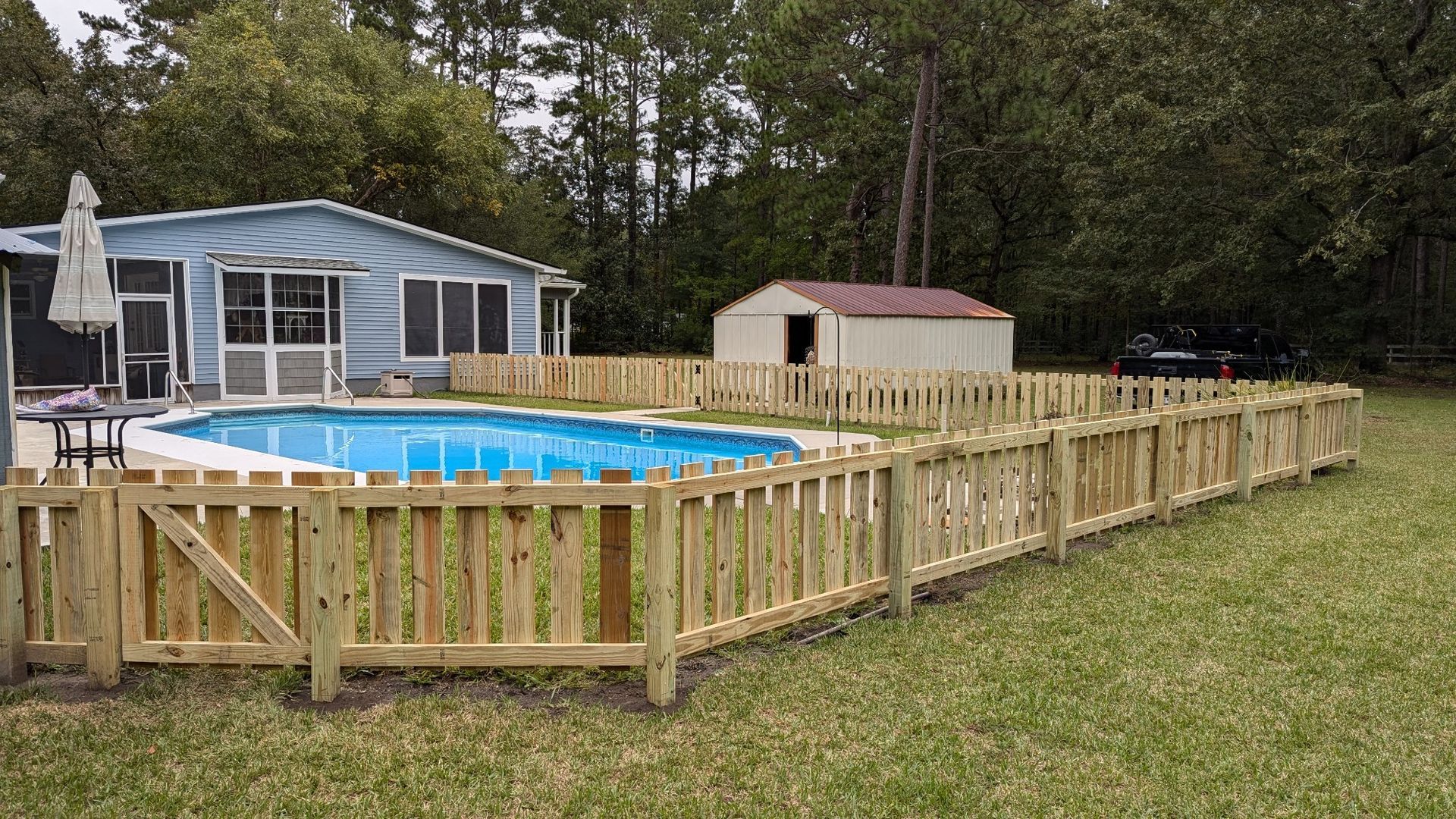 A wooden fence surrounds a swimming pool in front of a house.