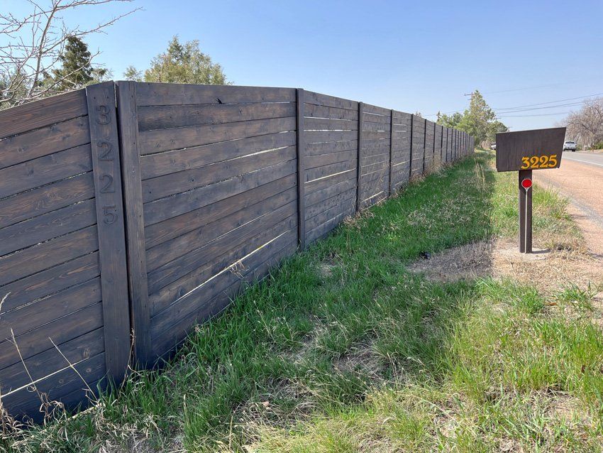 A wooden fence surrounds a grassy field next to a mailbox.