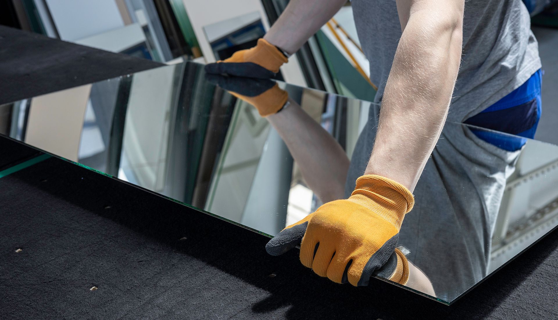 Person wearing gloves handling a large mirror, likely in a workshop.