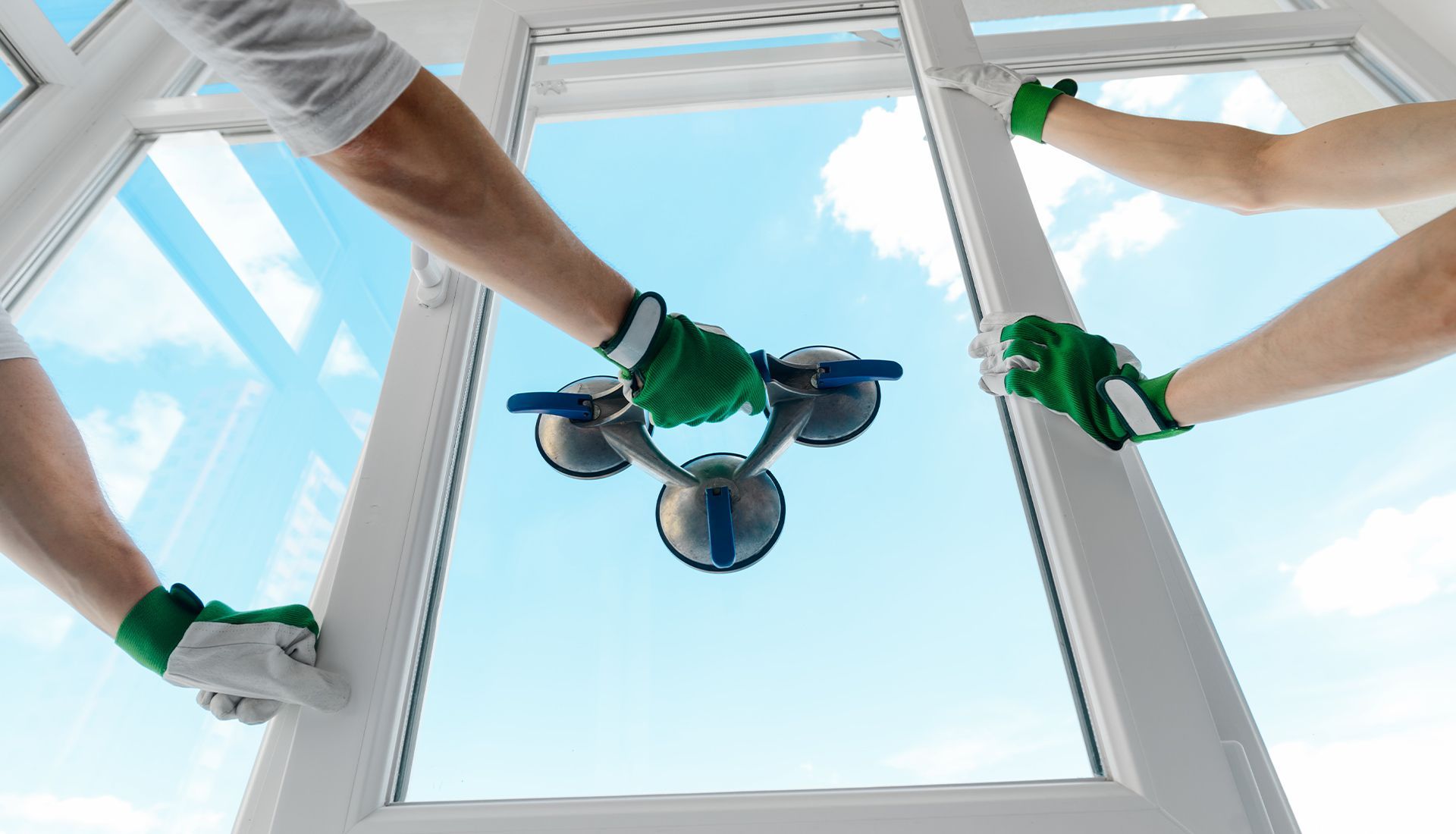Three people installing a window, using suction cups, blue sky visible through the opening.