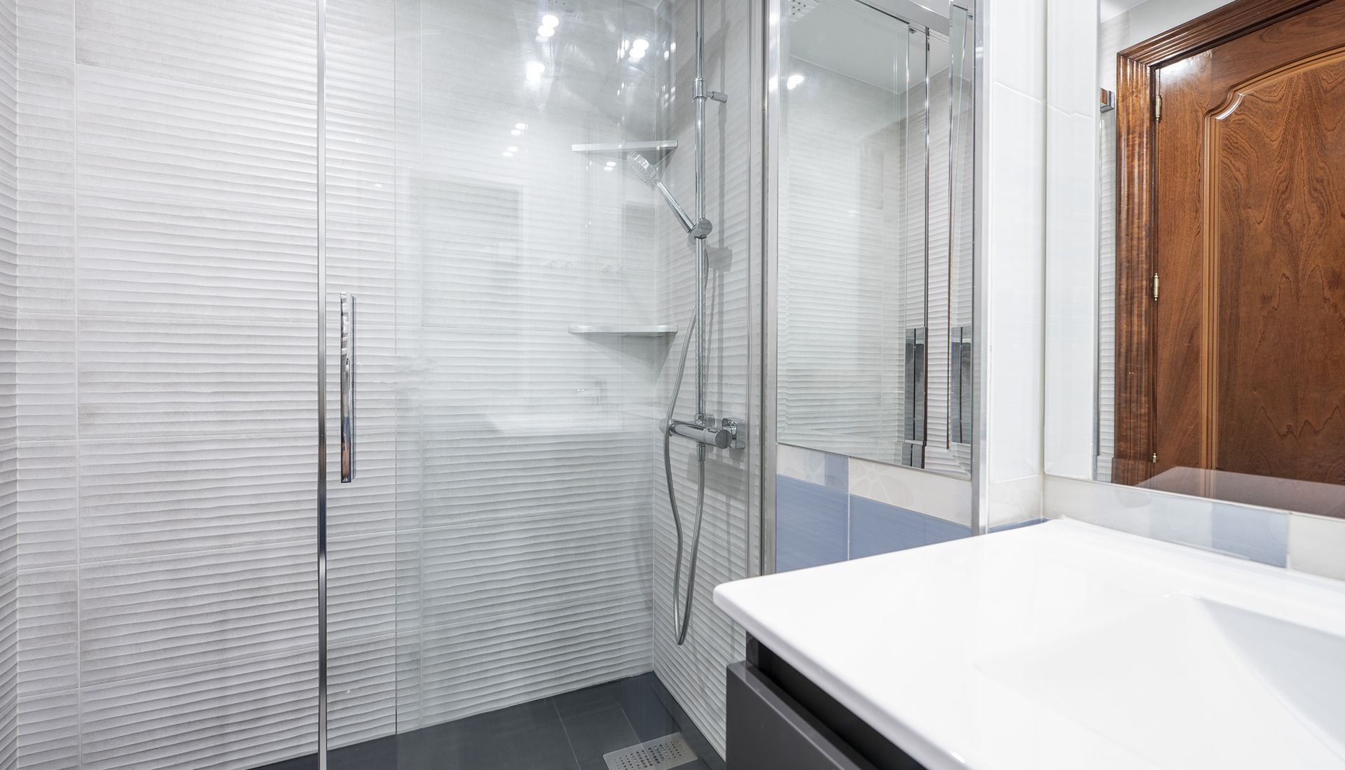 Modern bathroom with glass shower, white countertop, wooden door.
