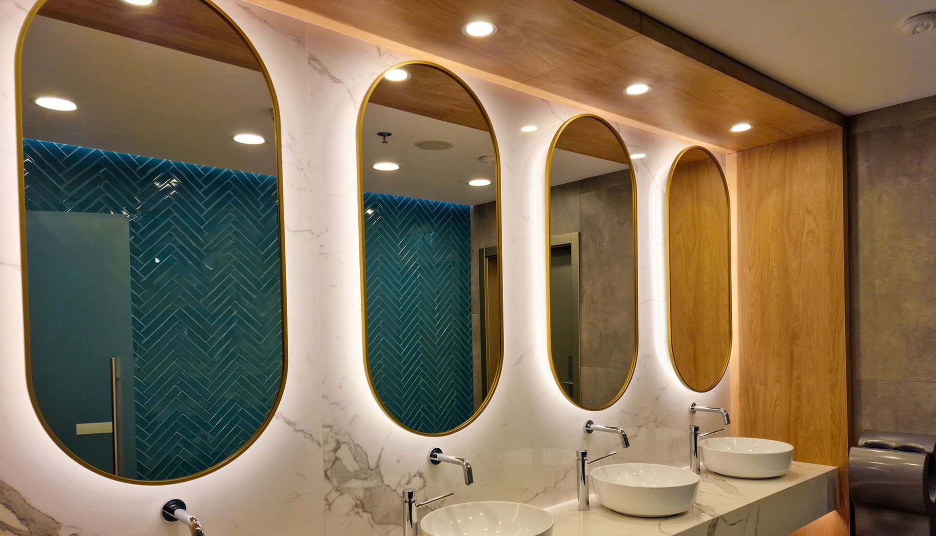 Stylish public restroom with oval mirrors, teal tiled walls, and marble countertops.