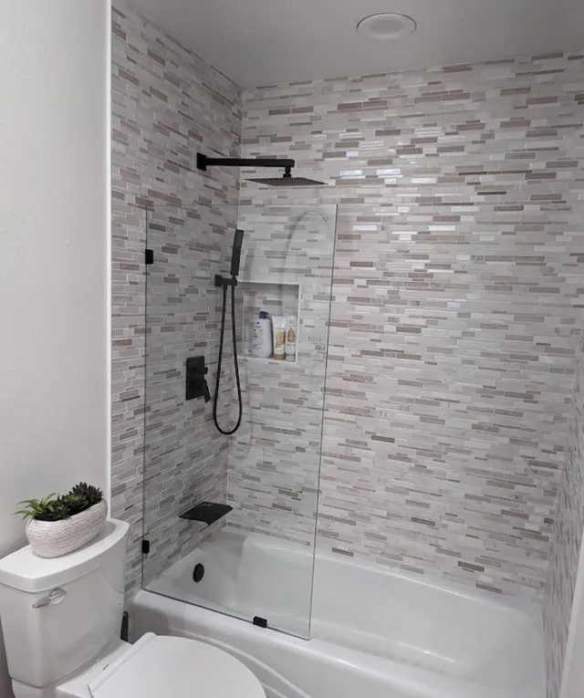 Bathroom with a bathtub and shower with glass door, light-colored stone-look tile, black shower fixtures.