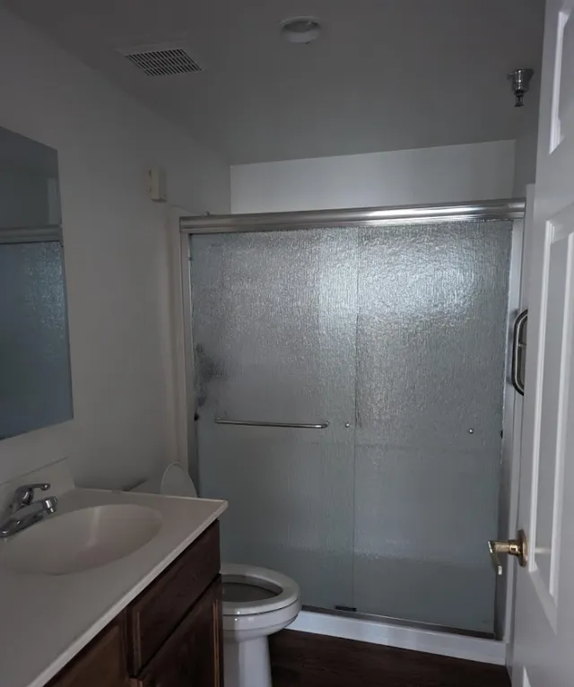 Bathroom with vanity, toilet, shower with frosted glass doors, and white walls.