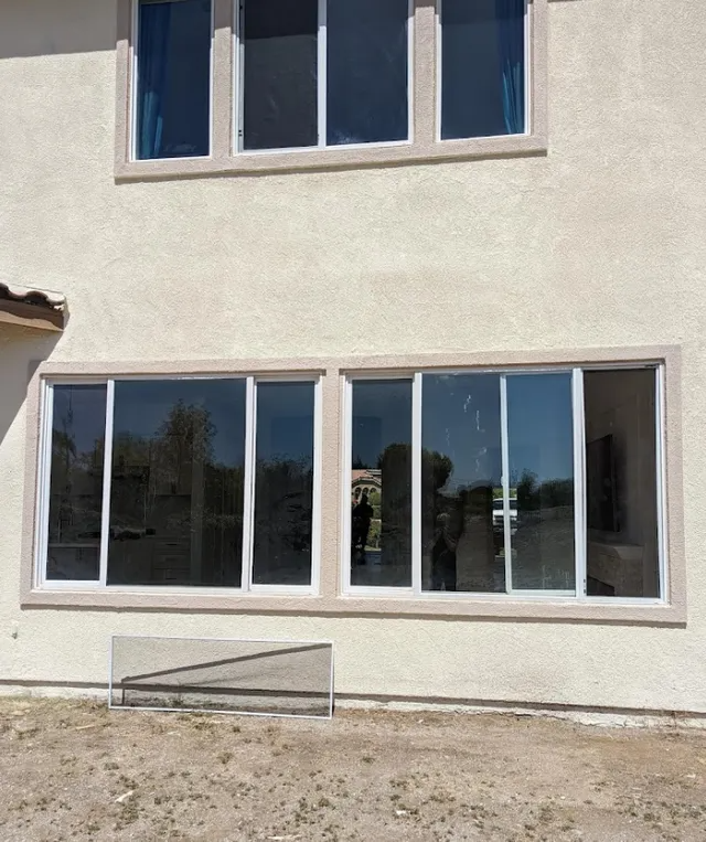 Two-story building exterior with large windows; beige stucco, white frames, and clear sky reflection.
