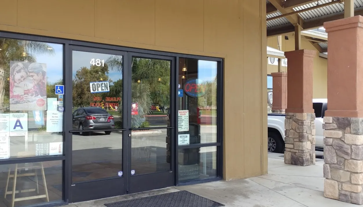 Exterior of a shop with glass doors, a tan facade, and stone columns. A car is visible through the doors.