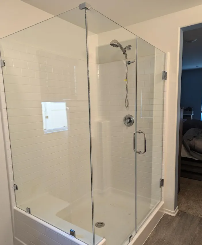 Glass shower enclosure in a bathroom, white tile, silver fixtures, and gray flooring.