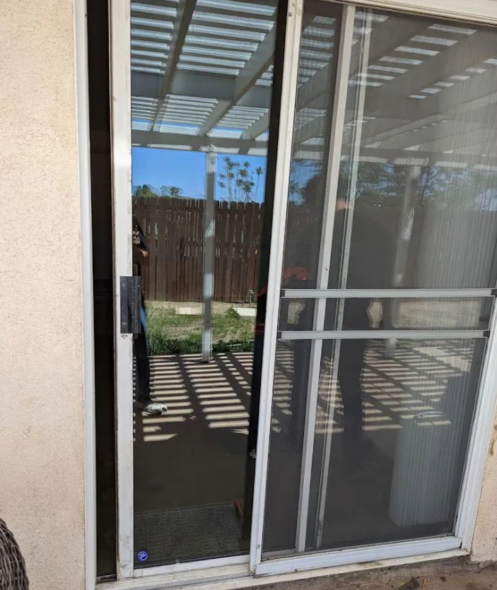 Sliding glass door partially open onto a backyard with a wooden fence and shadows.